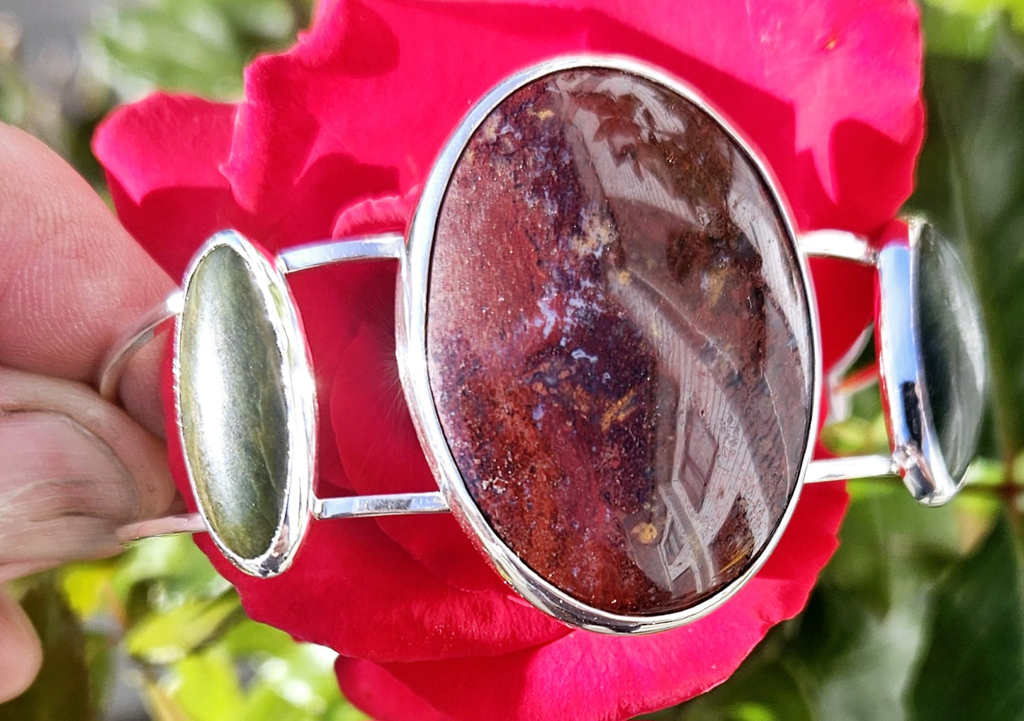Sterling silver cuff bracelet with 40x30mm New Zealand jasper, from the Hotoritori stream and hand polished with a pair of New Zealand Pounamu (nephrite jade) cabs accenting. Jasper from the Hotoritori stream is known for beautiful red colour with flecks of many other colours mixed in, flanking stone view