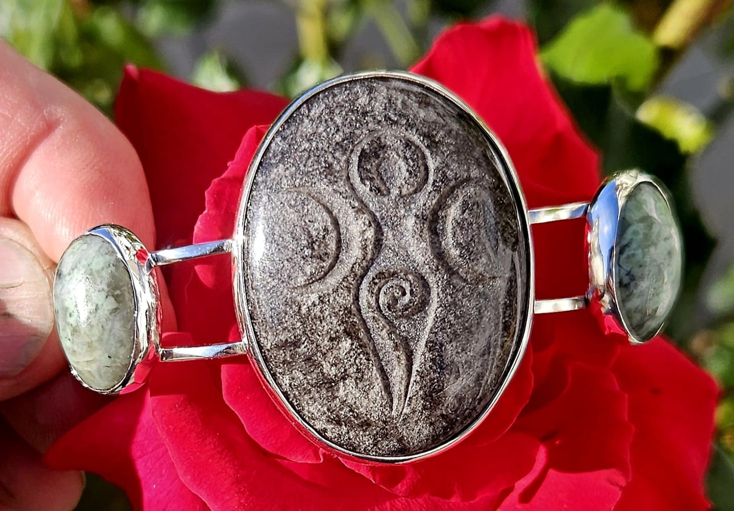 Sterling Silver Cuff bracelet with a 40x30mm cab of Taupo, New Zealand silver sheen obsidian, hand cut and engraved with a goddess symbol and flanked by 2 cabochons of New Zealand green grossular garnet, hand cut to 18x13mm cabs, main view.