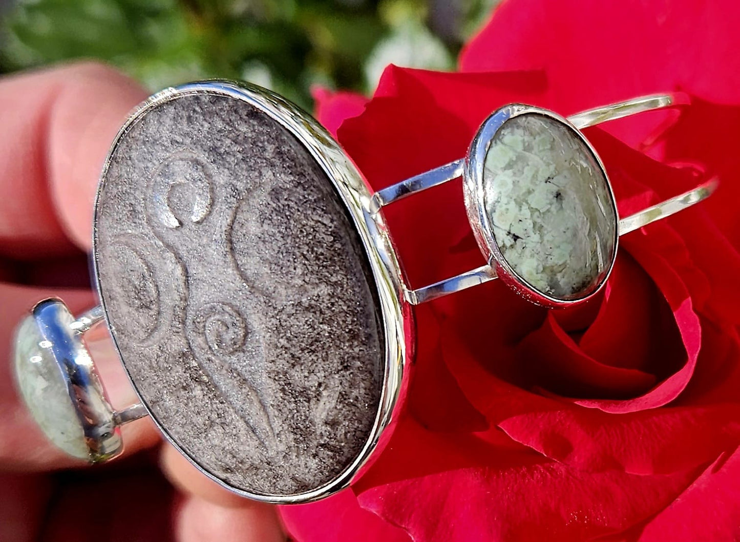 Sterling Silver Cuff bracelet with a 40x30mm cab of Taupo, New Zealand silver sheen obsidian, hand cut and engraved with a goddess symbol and flanked by 2 cabochons of New Zealand green grossular garnet, hand cut to 18x13mm cabs, angle view.
