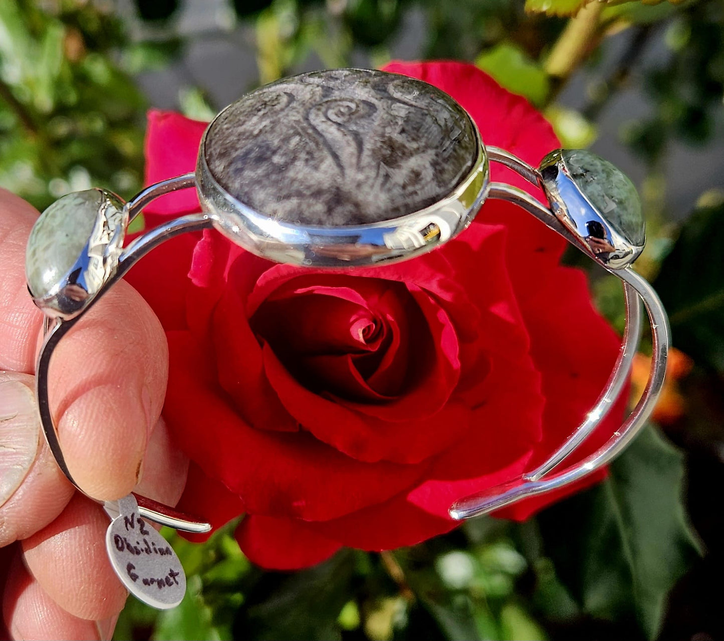 Sterling Silver Cuff bracelet with a 40x30mm cab of Taupo, New Zealand silver sheen obsidian, hand cut and engraved with a goddess symbol and flanked by 2 cabochons of New Zealand green grossular garnet, hand cut to 18x13mm cabs, side angle view.