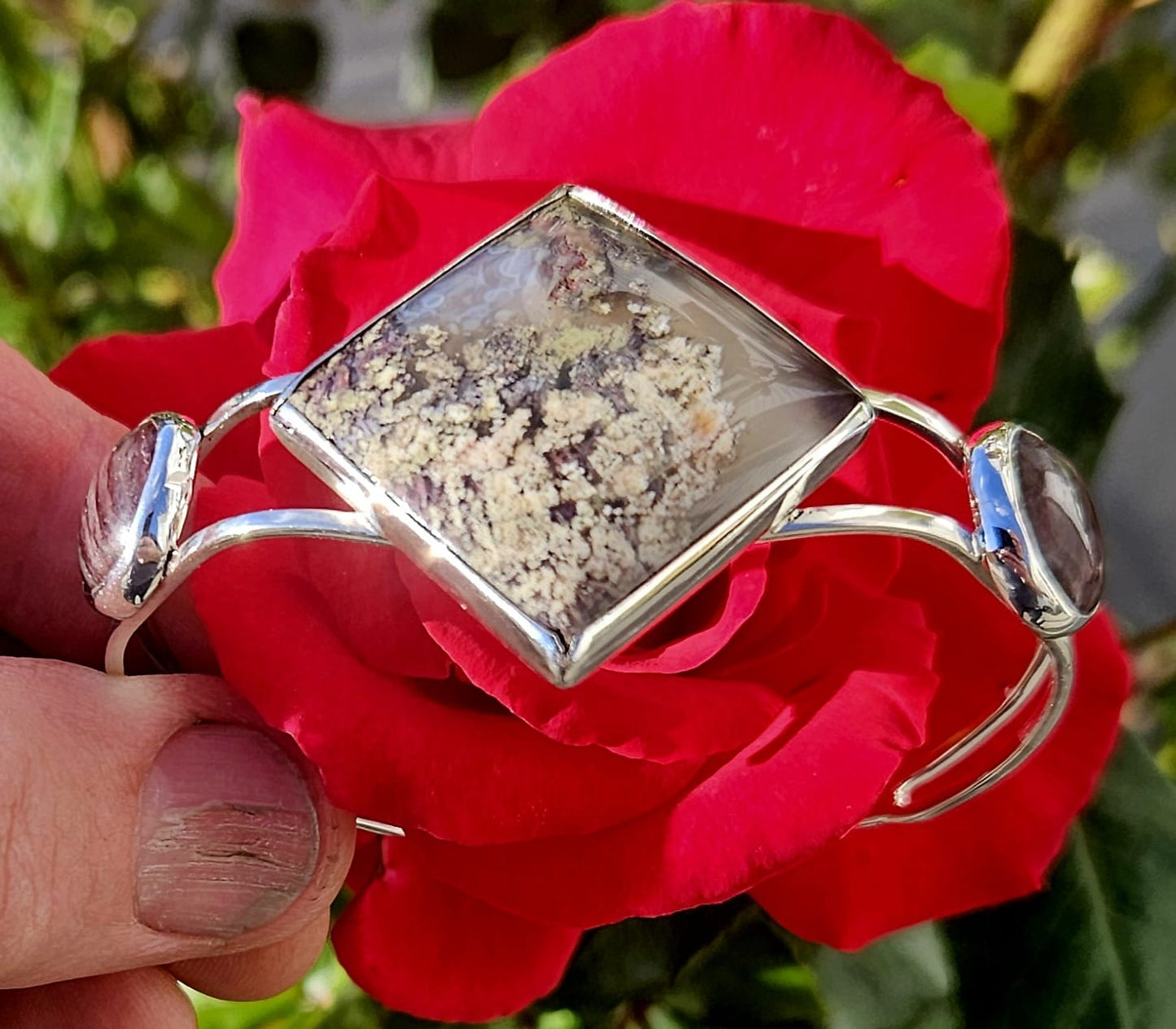 Sterling Silver Cuff bracelet with a 27x27mm square cabochon of Indonesian picture moss agate, flanked by a pair of purple New Zealand Aroha stones cut to 14mm round cabochons and set in sterling silver, side view.