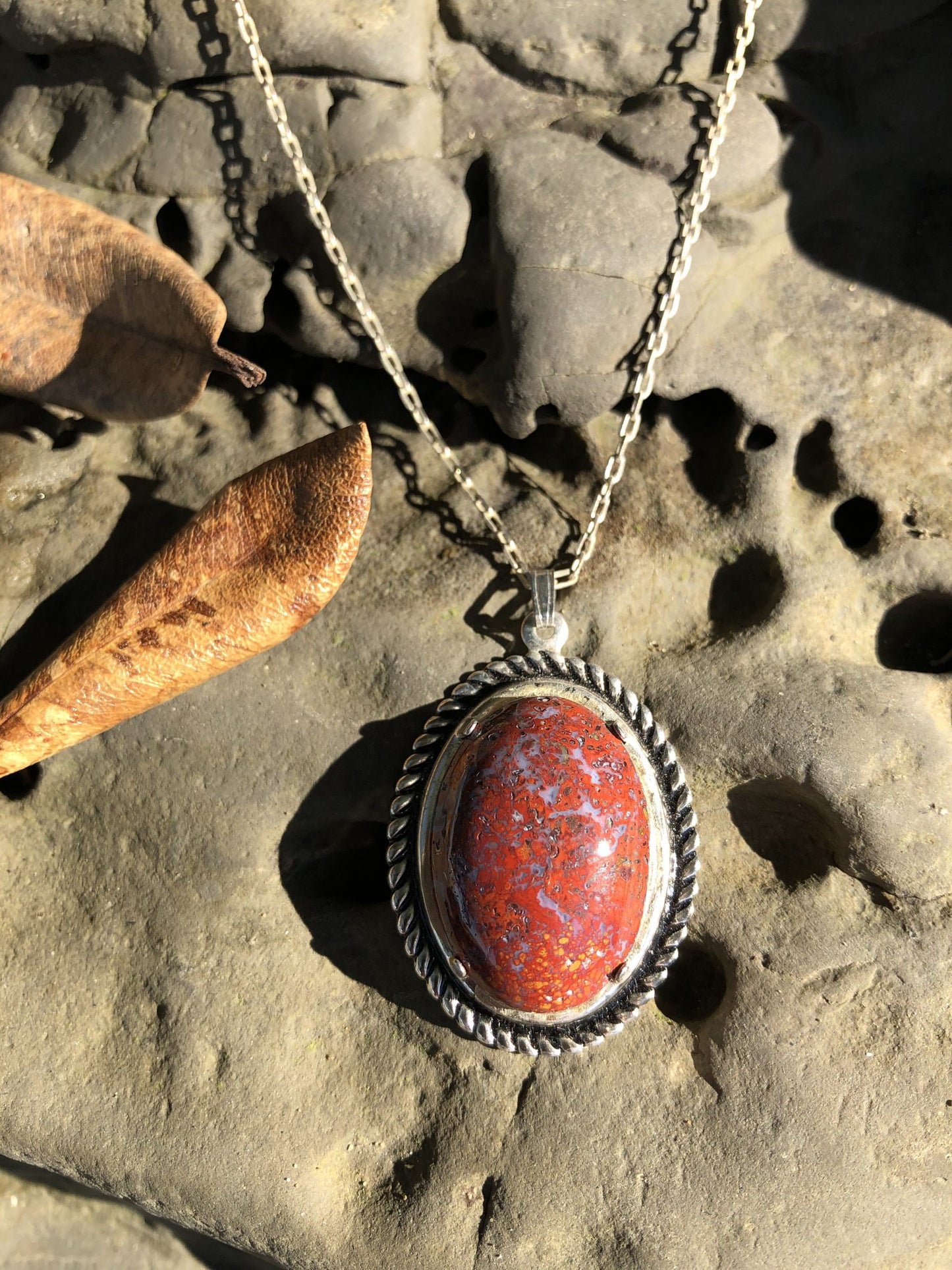 Necklace with New Zealand natural Chakra Jasper, luscious red with patterns of every color of the chakras, yellow, blue, black, orange, white patterns throughout, hand polished to a 25x18mm cabochon and set in a silver plated setting with 19 inch chain on stone