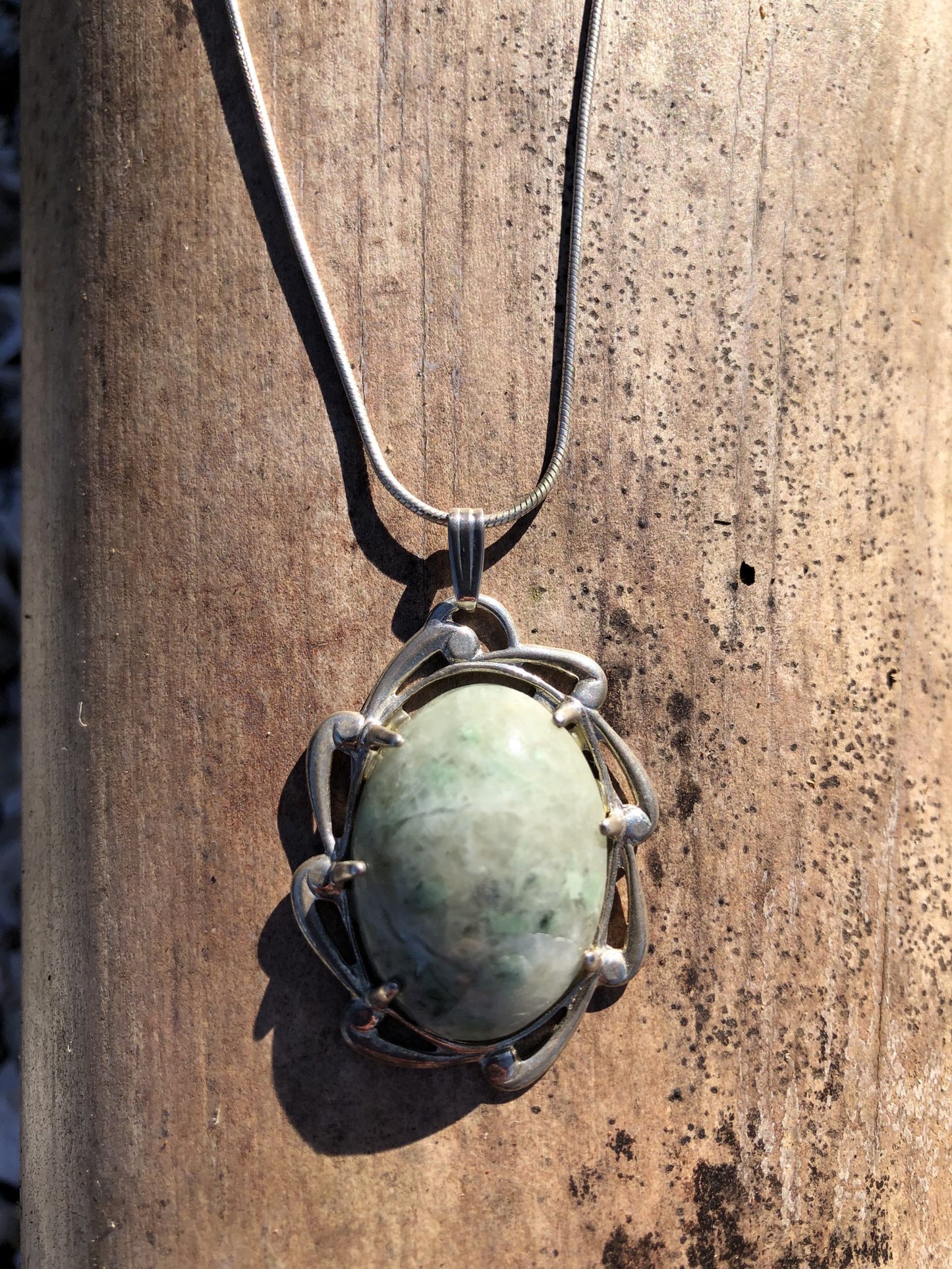 Necklace with New Zealand Hydrogrossular garnet green with white patterning from the Polaris River in Nelson and hand polished to a 25x18mm cabochon and set in sterling silver with a 24 inch sterling silver snake chain, on wood