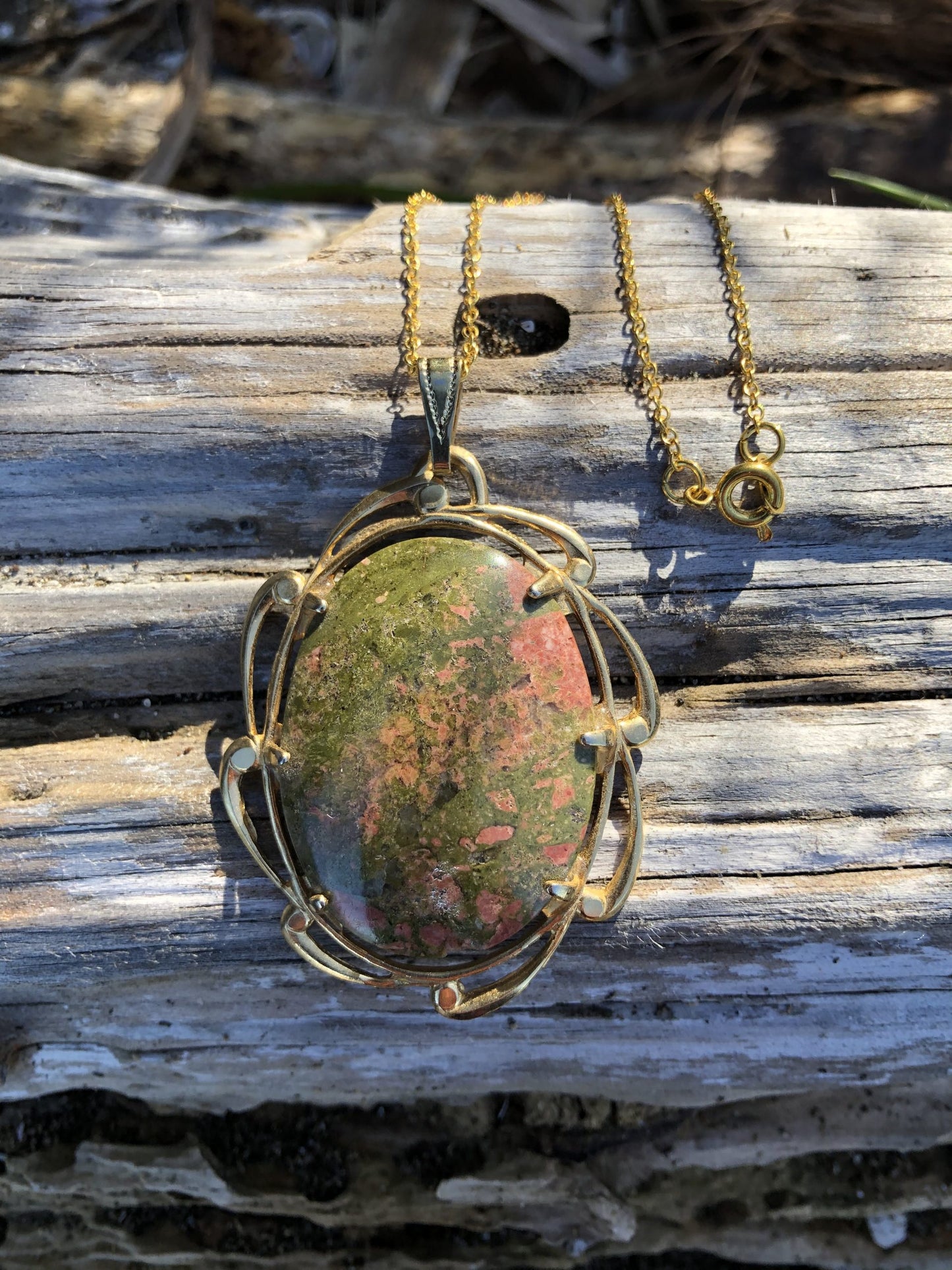 Necklace of green and pink unakite from South Island New Zealand, hand polished into a 40x30mm cabochon and set in gold plated setting with 19 inch chain. Unakite was descried as only found in Virginia USA for years until this deposit was discovered in New Zealand. This stone combines both the pink and green colours of the heart chakrah, pictured on log