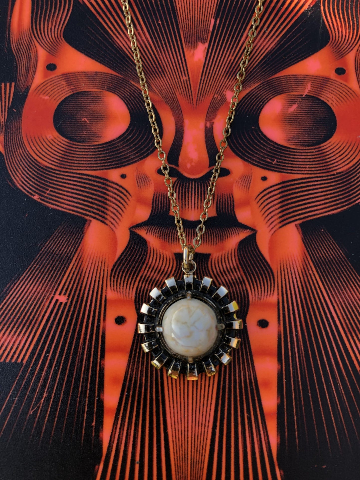 Necklace with natural New Zealand chert, white with gold lace patterns, hand polished to a 10mm round cabochon and set in a gold plated setting with 19 inch chain, on red art