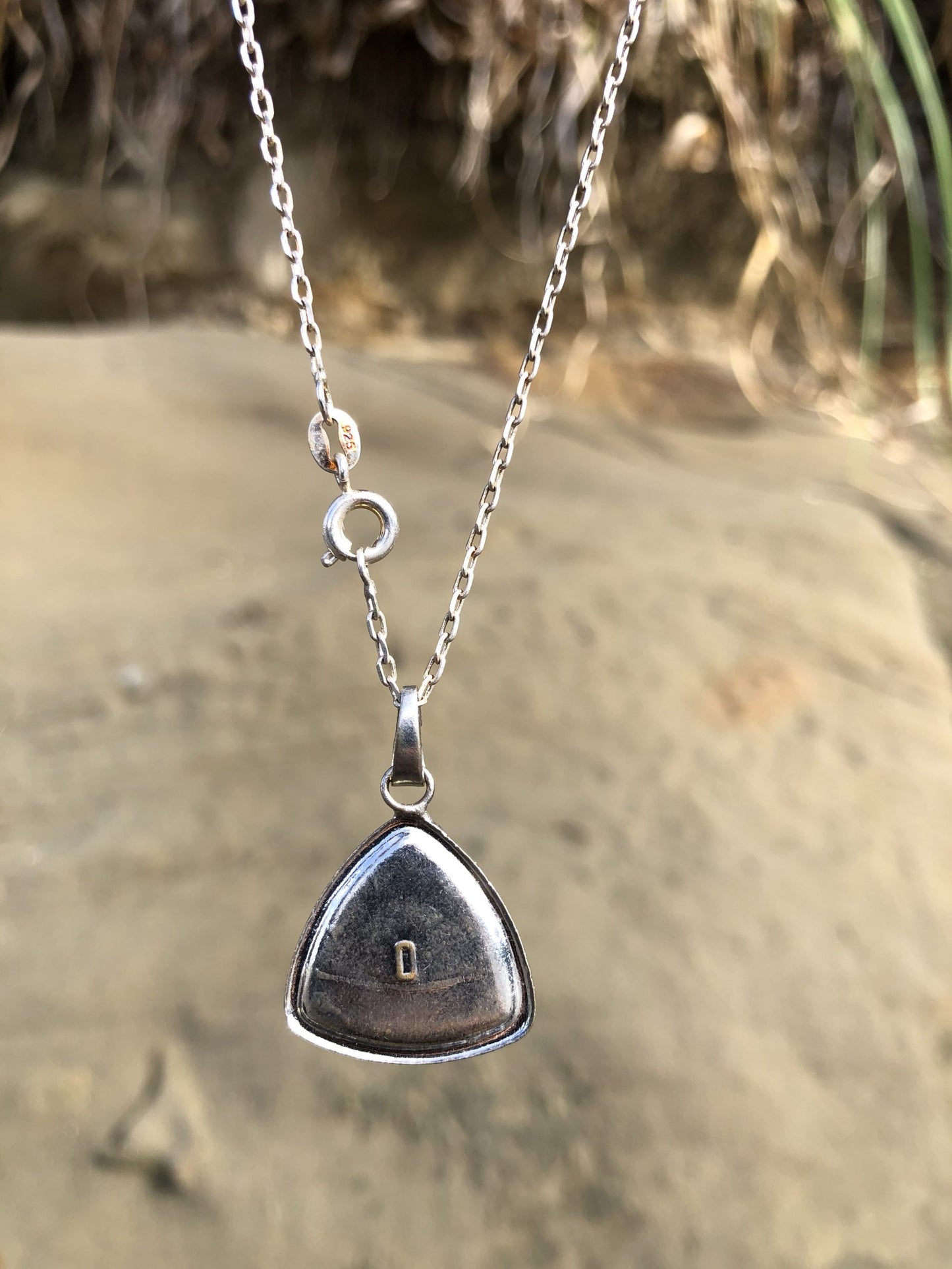 Necklace with New Zealand fossil stone from Hawkes Bay with white and black shell fossils in a gray background, hand polished to a 14mm round cabochon and set in a silver plated setting with 19 inch chain, back