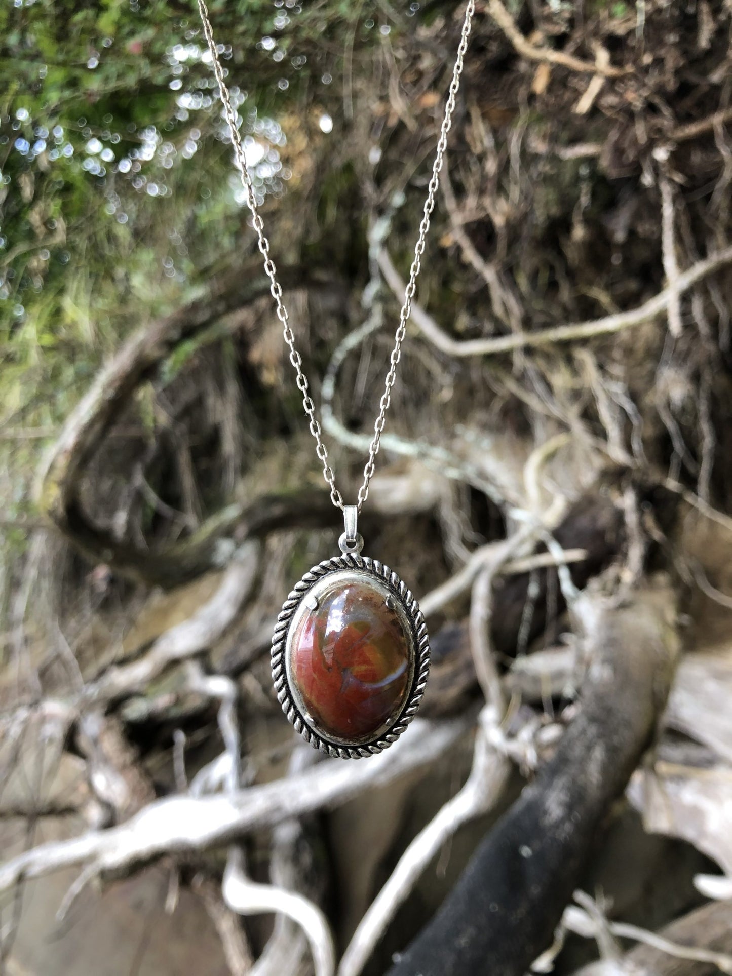 Necklace with New Zealand Chakra Jasper, hand polished to a 25x18mm cabochon and set in a silver plated setting with 19 inch chain. Chakra jasper is a special form of jasper found in New Zealand that contains all (or most) of the chakra stone within it. This stone is predominantly red with orange, yellow, green, blue, brown, black and white, further