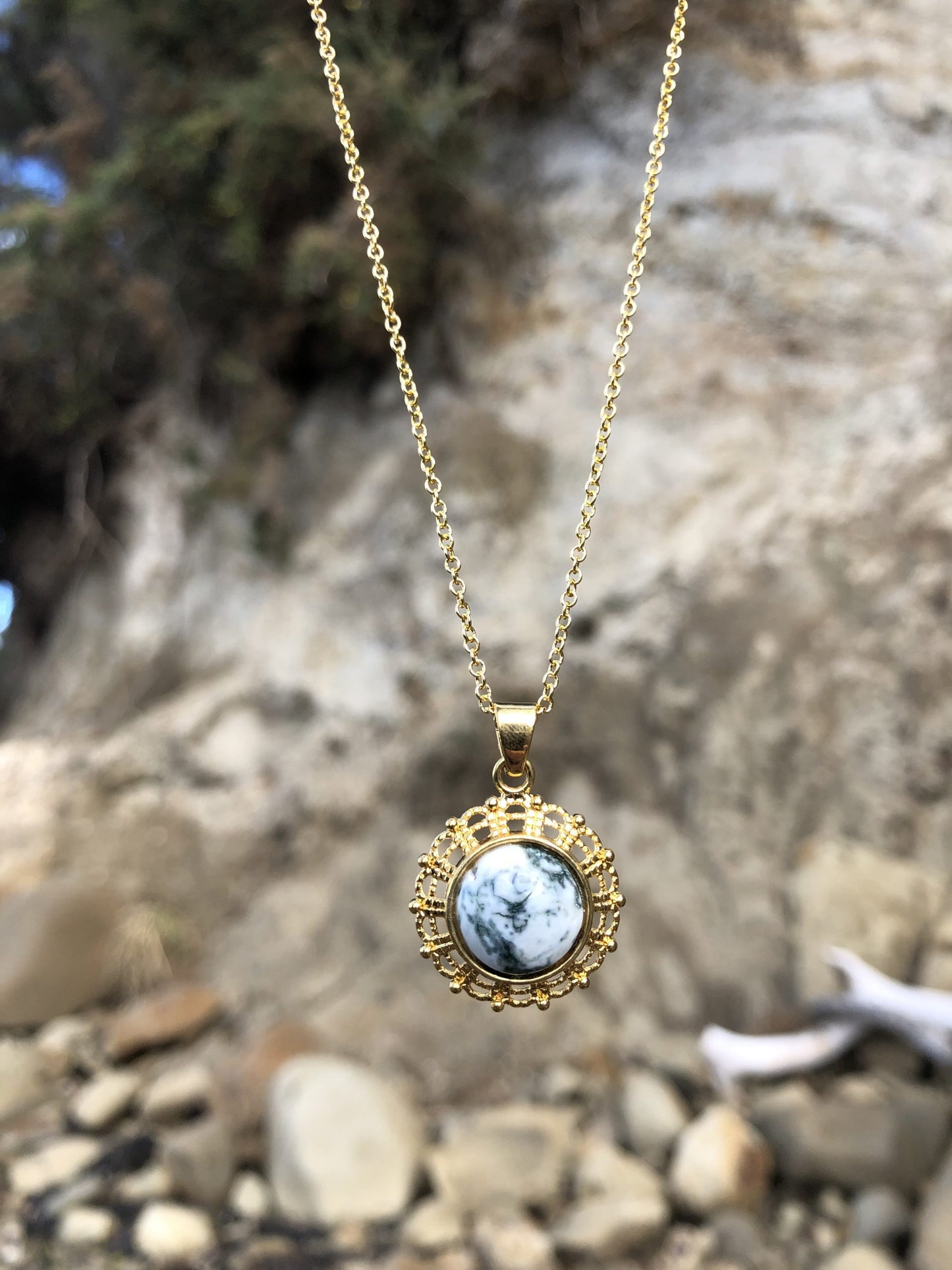 Necklace with natural Tree Agate, a unique type of moss agate with a white background behind fine green "moss". The stone is hand polished to a 10mm round cabochon and set in a gold-plated setting with 19 inch chain, on beach