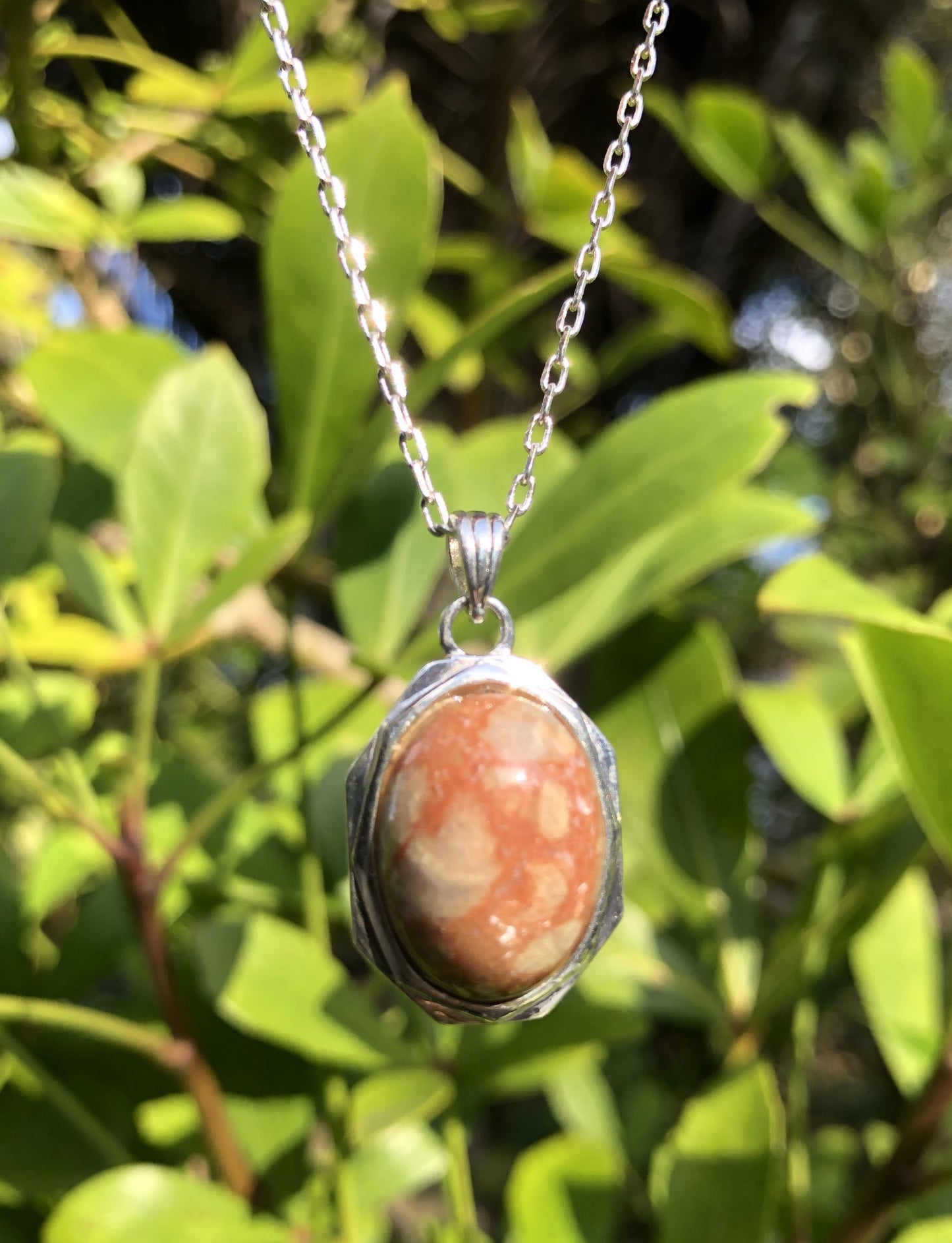 Necklace with Australian Peanut Stone showing cream-white spots in an orange-brown background, hand polished to a 18x13mm cabochon and set in a silver-plated setting with 19 inch chain.