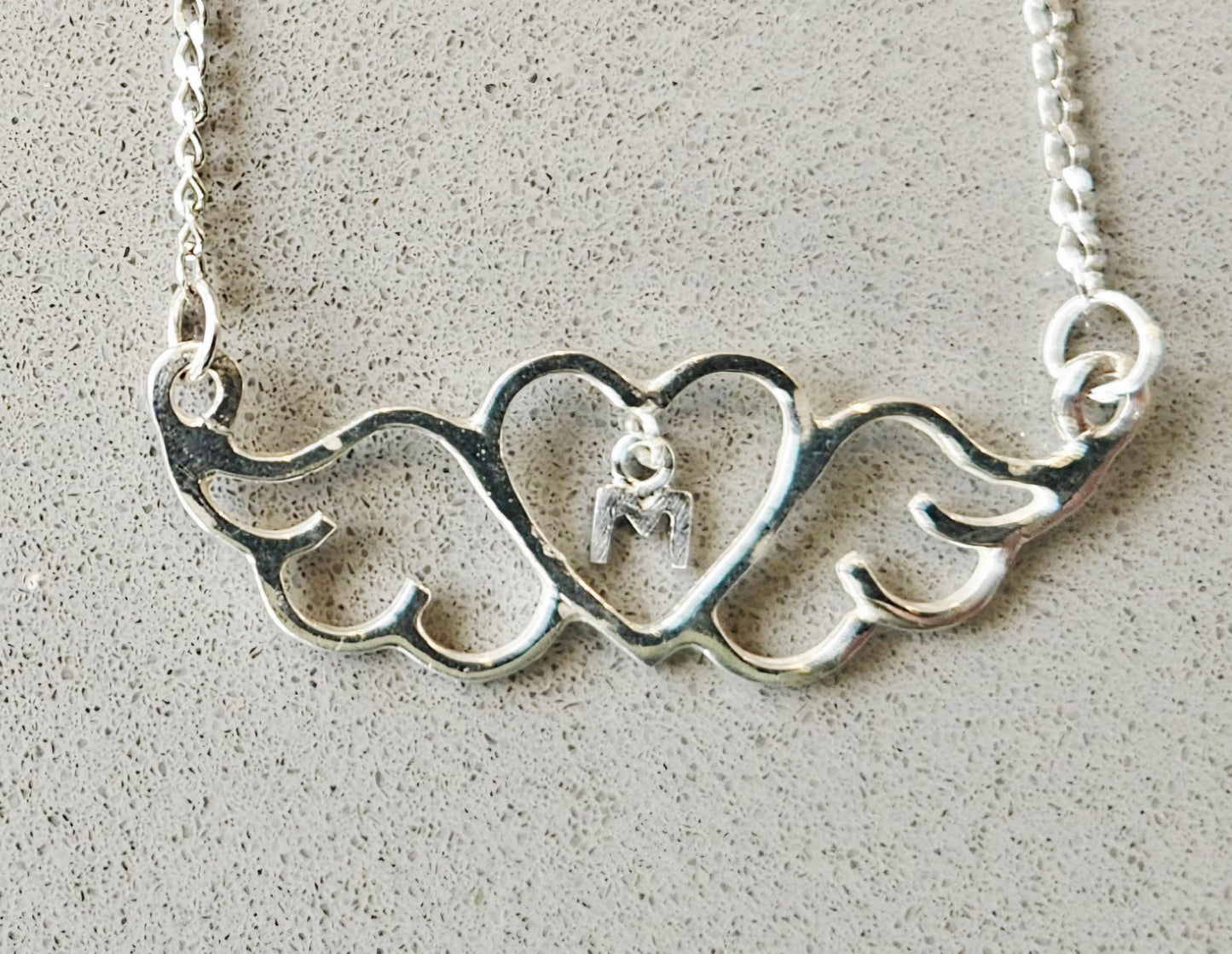Silver necklace with heart and wing design on a textured surface