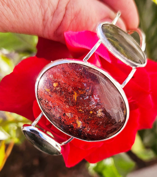 Sterling silver cuff bracelet with 40x30mm New Zealand jasper, from the Hotoritori stream and hand polished with a pair of New Zealand Pounamu (nephrite jade) cabs accenting. Jasper from the Hotoritori stream is known for beautiful red colour with flecks of many other colours mixed in, top view