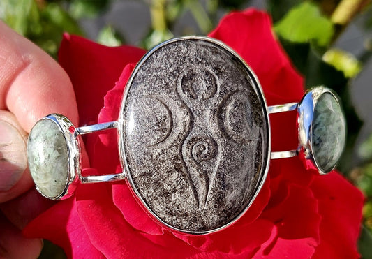 Sterling Silver Cuff bracelet with a 40x30mm cab of Taupo, New Zealand silver sheen obsidian, hand cut and engraved with a goddess symbol and flanked by 2 cabochons of New Zealand green grossular garnet, hand cut to 18x13mm cabs, main view.