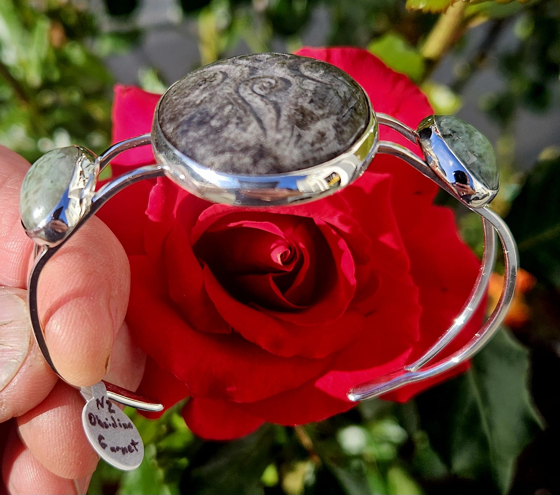 Sterling Silver Cuff bracelet with a 40x30mm cab of Taupo, New Zealand silver sheen obsidian, hand cut and engraved with a goddess symbol and flanked by 2 cabochons of New Zealand green grossular garnet, hand cut to 18x13mm cabs, side angle view.