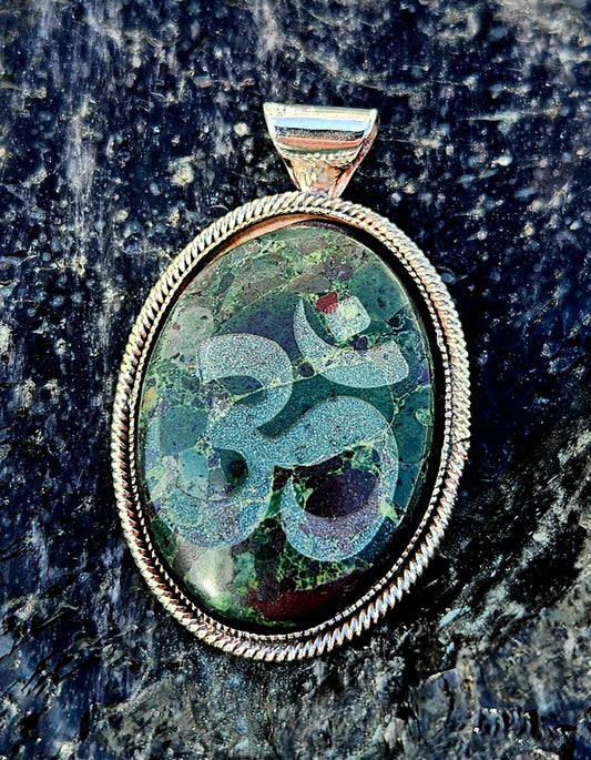 Necklace with a New Zealand multi-coloured rhyolite, hand polished to a 30x22mm cabochon with the Ohm symbol carved into the surface. This beautiful stone is set in a sterling silver setting with a 19 inch sterling silver chain, front.