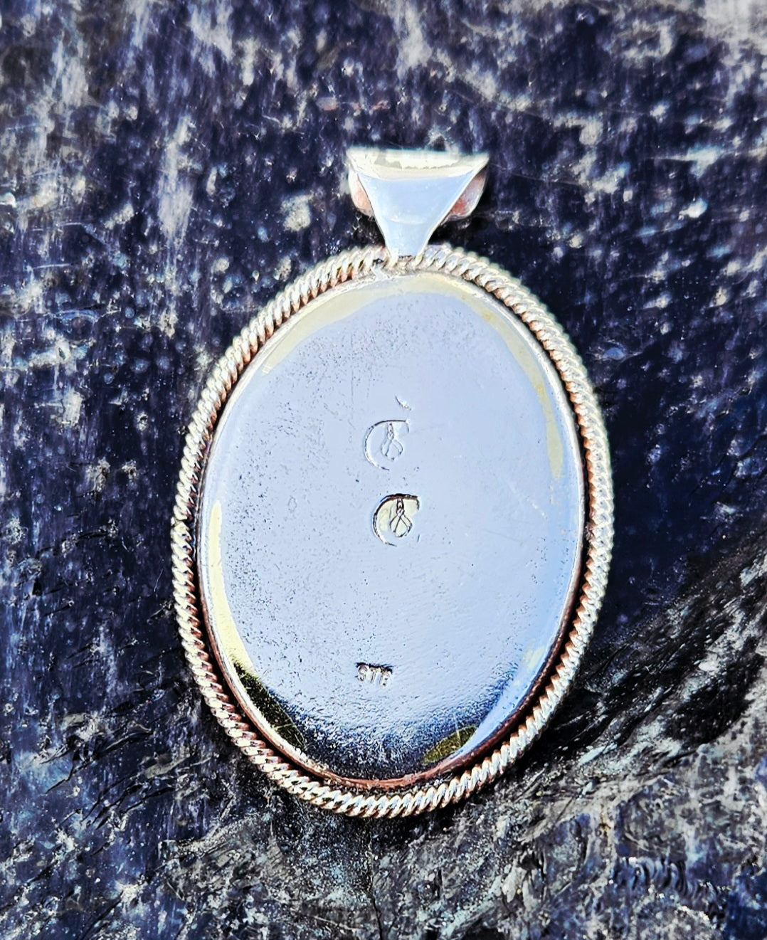 Necklace with a New Zealand multi-coloured rhyolite, hand polished to a 30x22mm cabochon with the Ohm symbol carved into the surface. This beautiful stone is set in a sterling silver setting with a 19 inch sterling silver chain, back.