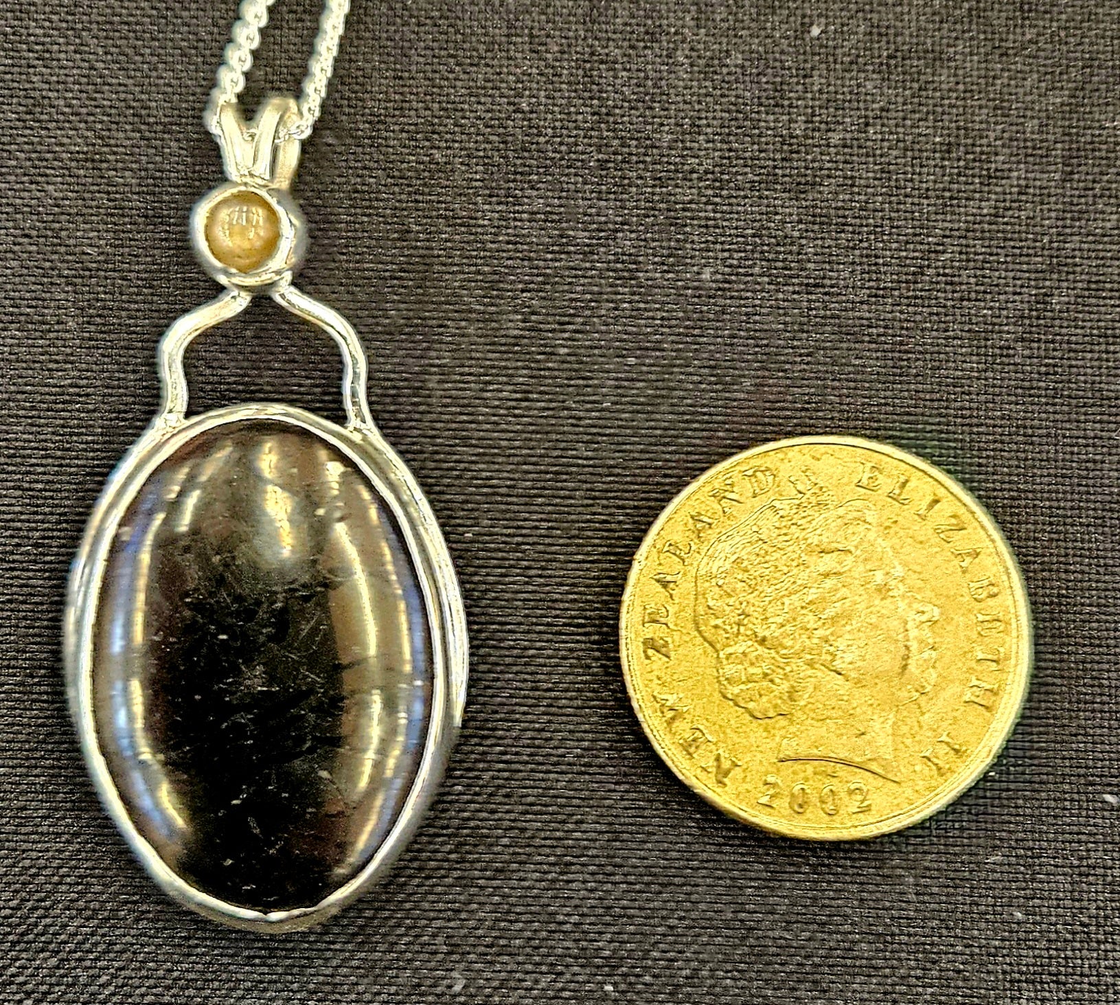 Shungite pendant with Moonstone accent in sterling silver and 18 inch sterling silver chain, with NZ one dollar coin for size comparison.