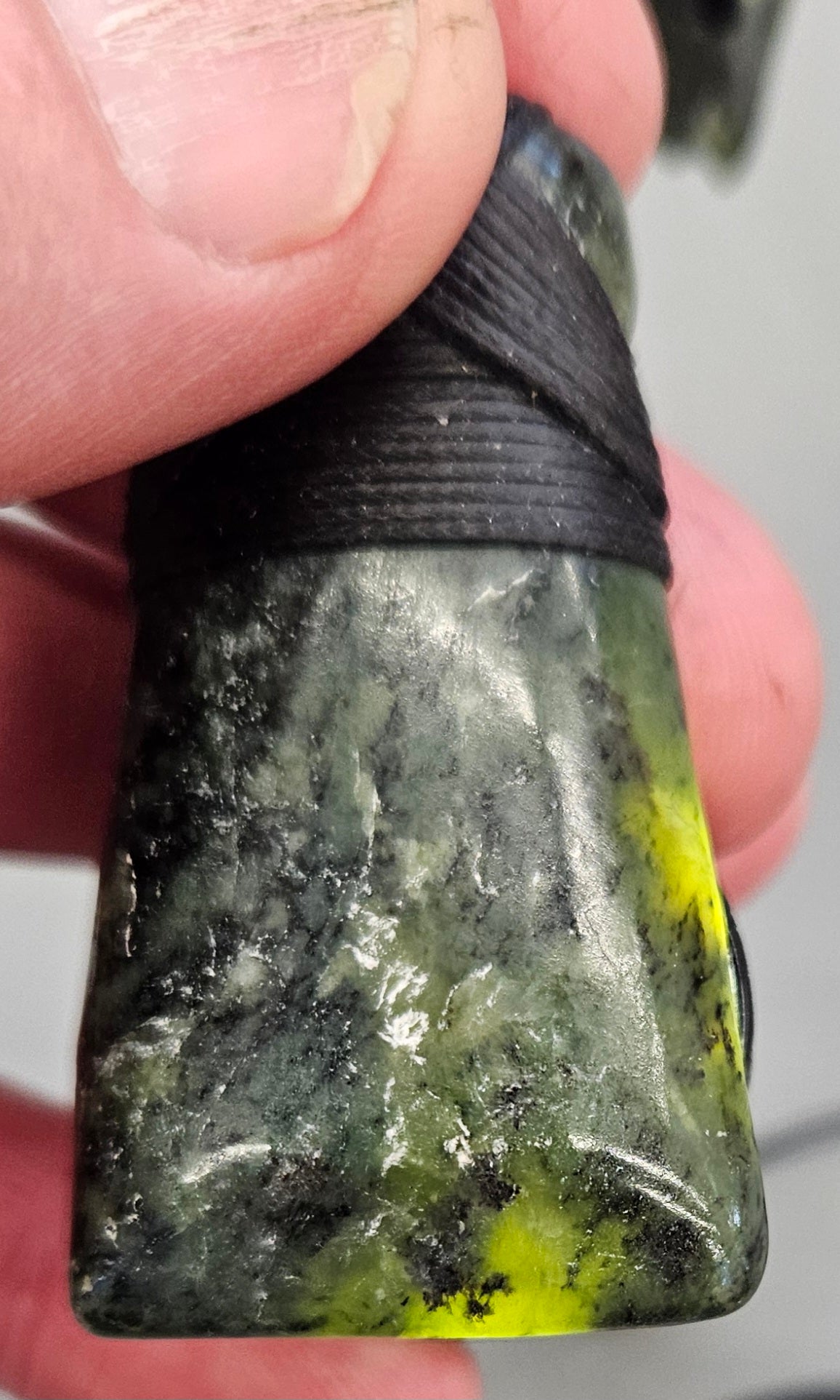 Kawakawa New Zealand Pounamu Toki, medium size, hand made with hand braided chord and NZ Pounamu toggle, back-lit to show stone transluscence.