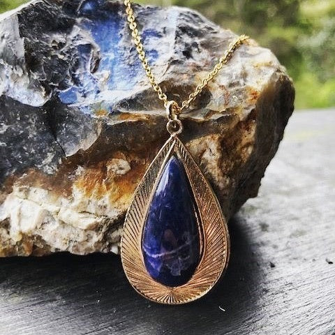 Necklace with natural blue sodalite with delicate white lace patterning, hand polished to a 27x13mm teardrop cabochon and set in a gold plated setting with 19 inch chain.