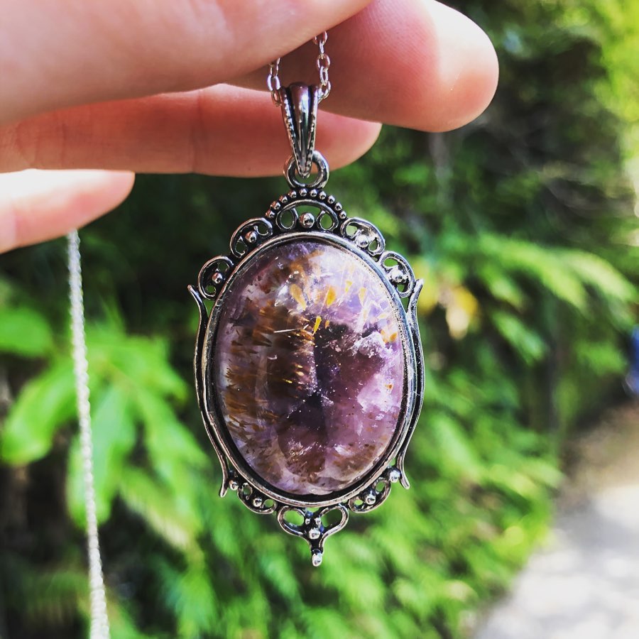 Necklace with natural Super-7, a rich purple amethyst with golden needles of cacoxenite, hand polished to a 30x22mm cabochon and set in silver plated setting with 19 inch chain