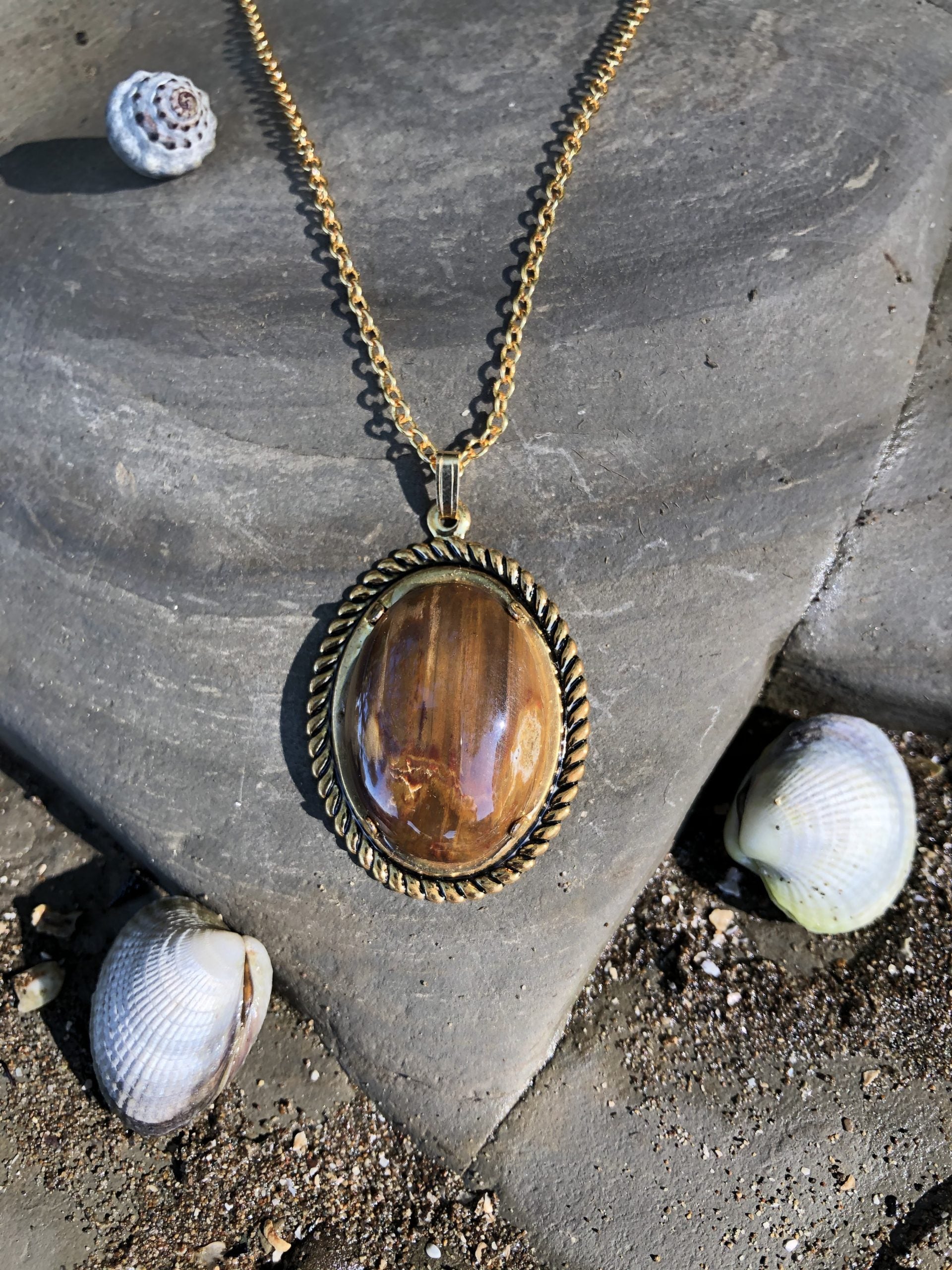 Necklace with Australian petrified wood showing beautiful grain patterns in lovely wood-tones of brown and tan, hand polished to a 25x18mm cabochon and set in a gold plated setting with 19 inch chain, close