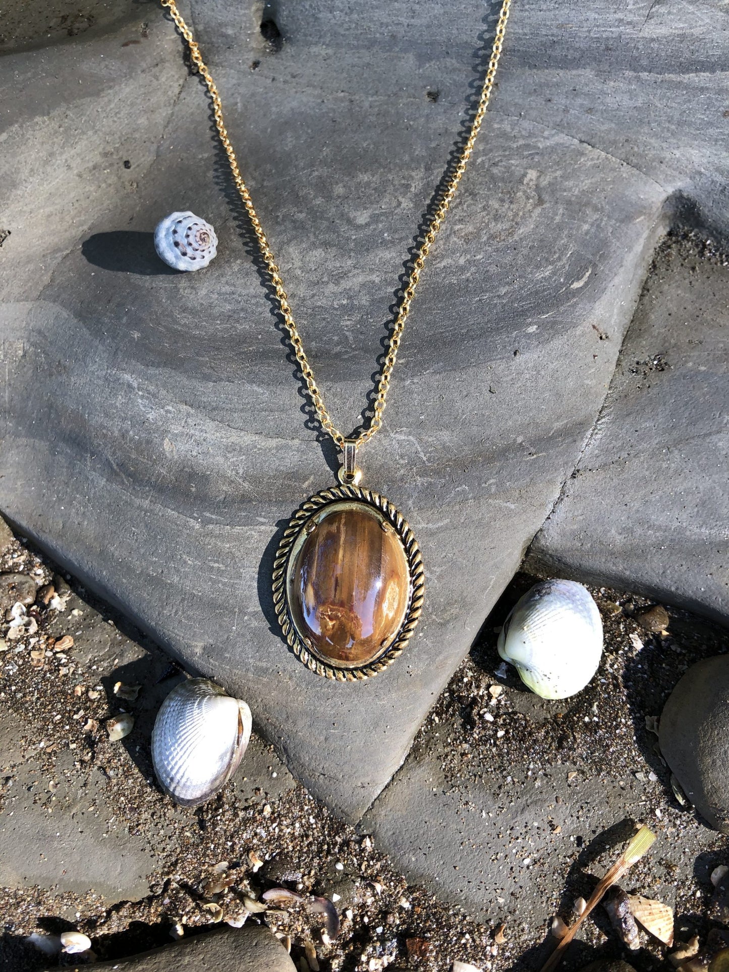 Necklace with Australian petrified wood showing beautiful grain patterns in lovely wood-tones of brown and tan, hand polished to a 25x18mm cabochon and set in a gold plated setting with 19 inch chain, distant