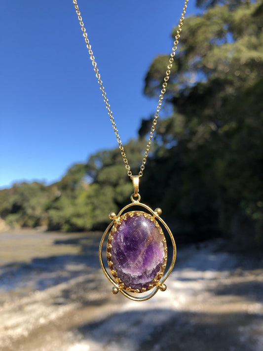 Necklace with rich, dark purple Amethyst, hand polished to a 30x22mm oval cabochon and set in a gold plated setting with 19 inch chain on beach