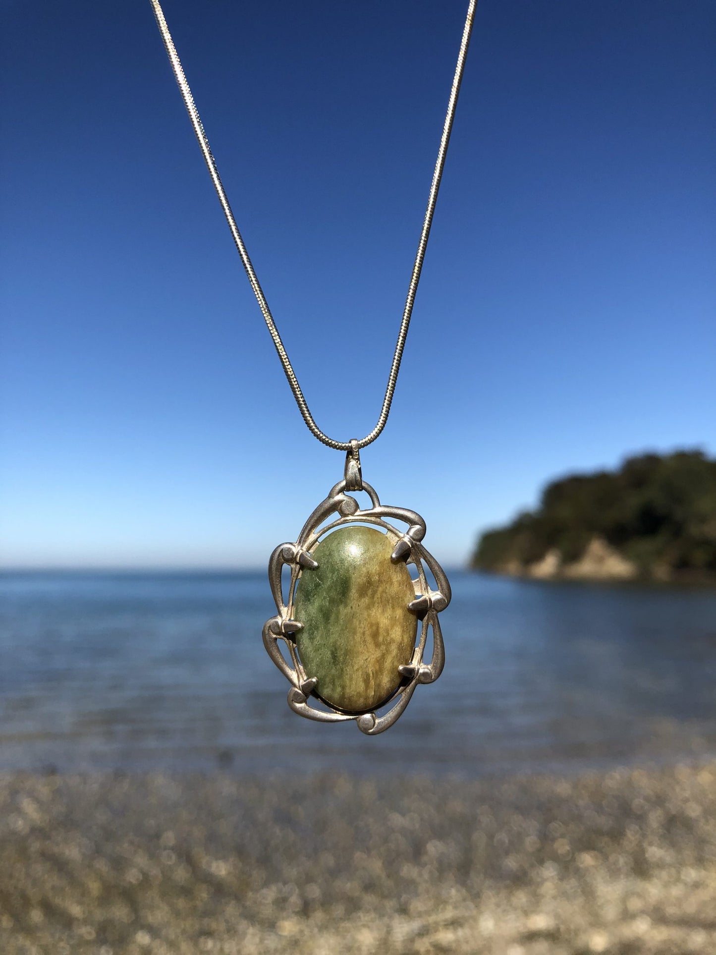 Necklace with New Zealand Marsden Flower jade (greenstone or Pounamu) with green and yellow markings, hand polished to a 25x18mm cabochon and set in sterling silver with 24 inch sterling silver snake chain on beach