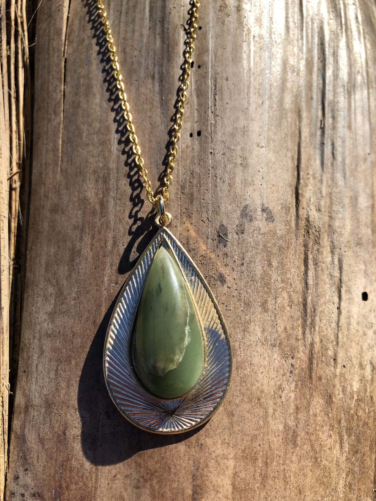 Necklace with natural Botswana Jade (green aventurine) stone, hand polished to a 32x12mm teardrop cabochon and set in a gold plated setting with 19 inch chain, on wood