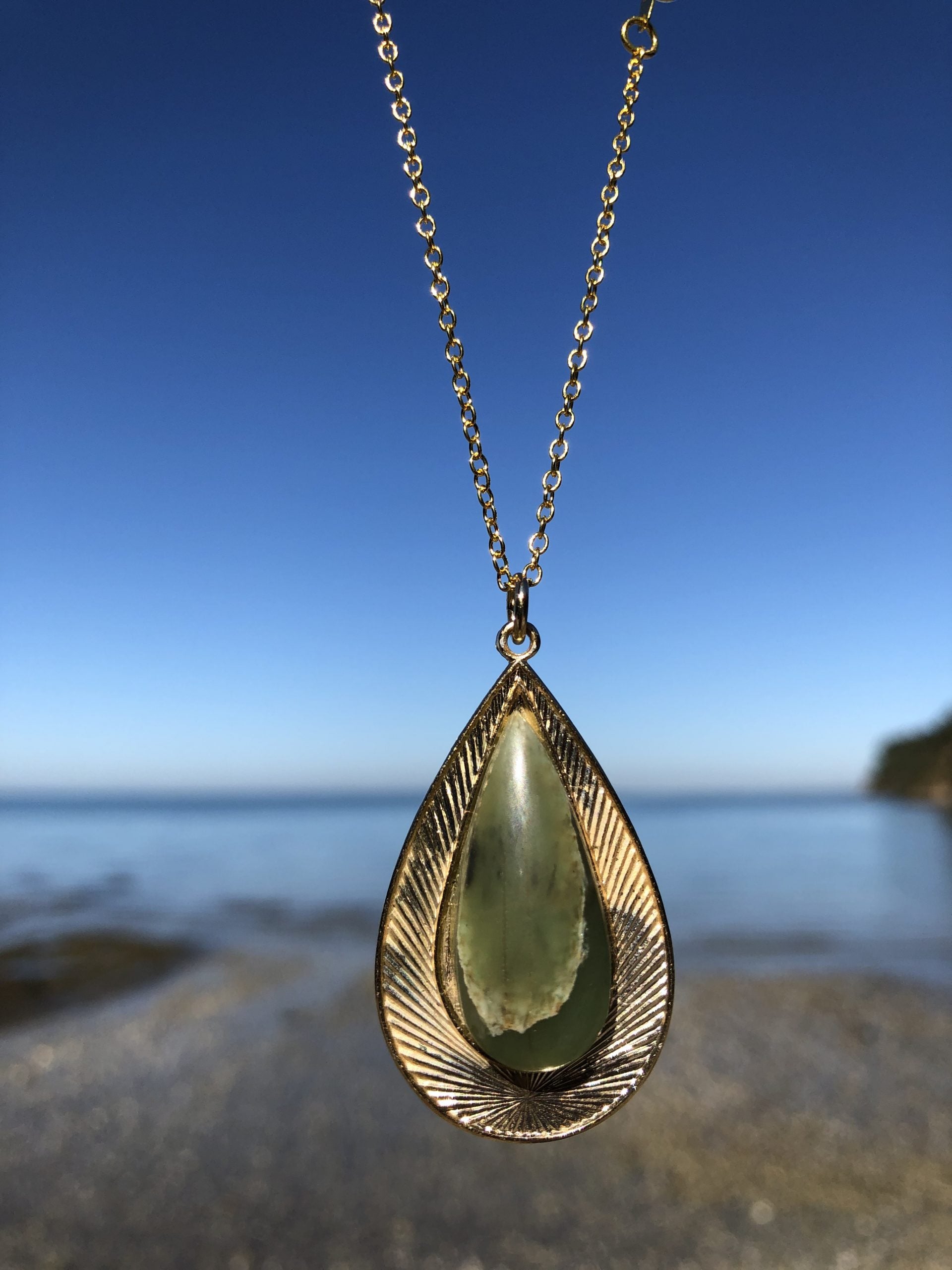 Necklace with natural Botswana Jade (green aventurine) stone, hand polished to a 32x12mm teardrop cabochon and set in a gold plated setting with 19 inch chain, on beach