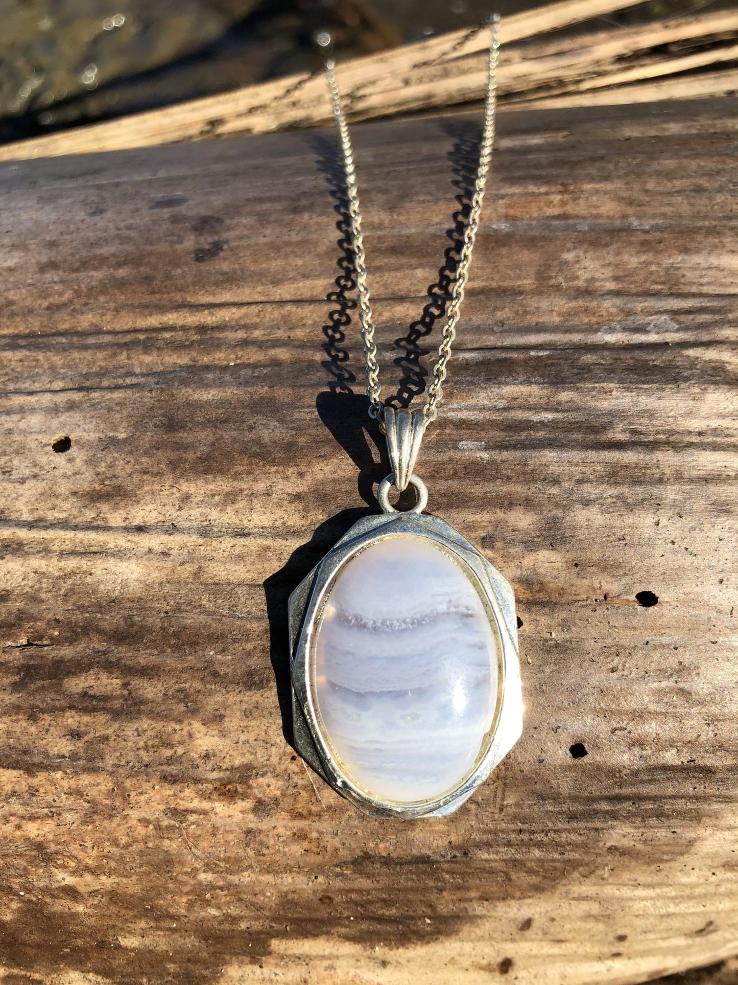 Necklace of Namibian Blue Lace Agate, with delicate blue and white stripes, hand polished to a 25x18mm cabochon and set in silver plated setting with 19 inch chain, on wood