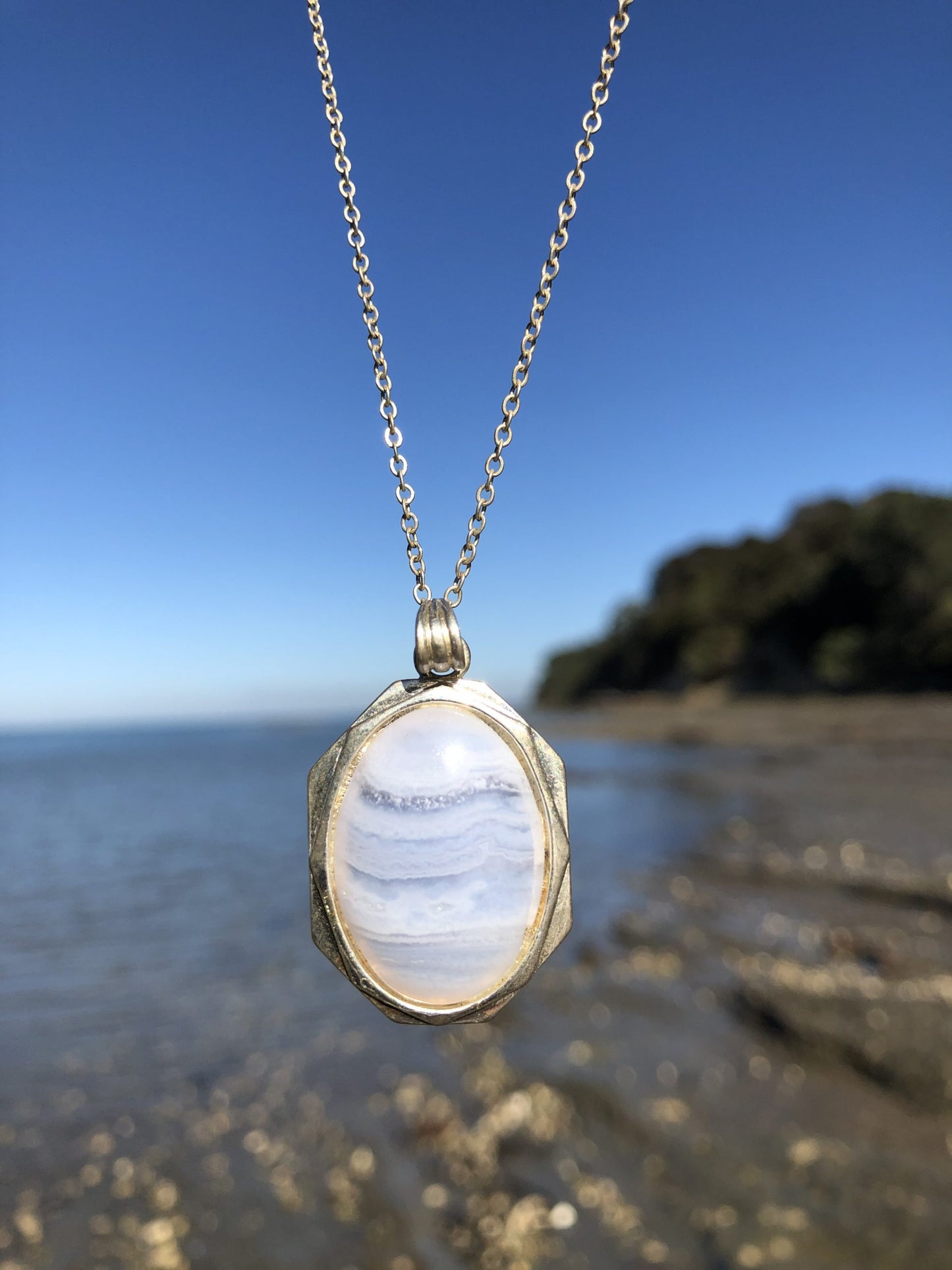Necklace of Namibian Blue Lace Agate, with delicate blue and white stripes, hand polished to a 25x18mm cabochon and set in silver plated setting with 19 inch chain, on beach