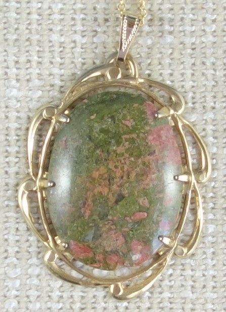 Necklace of green and pink unakite from South Island New Zealand, hand polished into a 40x30mm cabochon and set in gold plated setting with 19 inch chain. Unakite was descried as only found in Virginia USA for years until this deposit was discovered in New Zealand. This stone combines both the pink and green colours of the heart chakrah, pictured on burlap