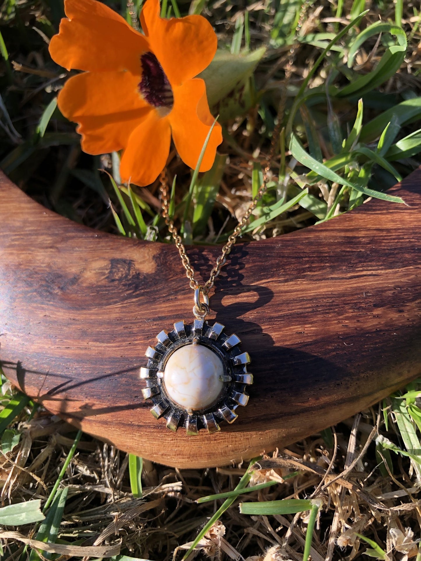 Necklace with natural New Zealand chert, white with gold lace patterns, hand polished to a 10mm round cabochon and set in a gold plated setting with 19 inch chain, on wood