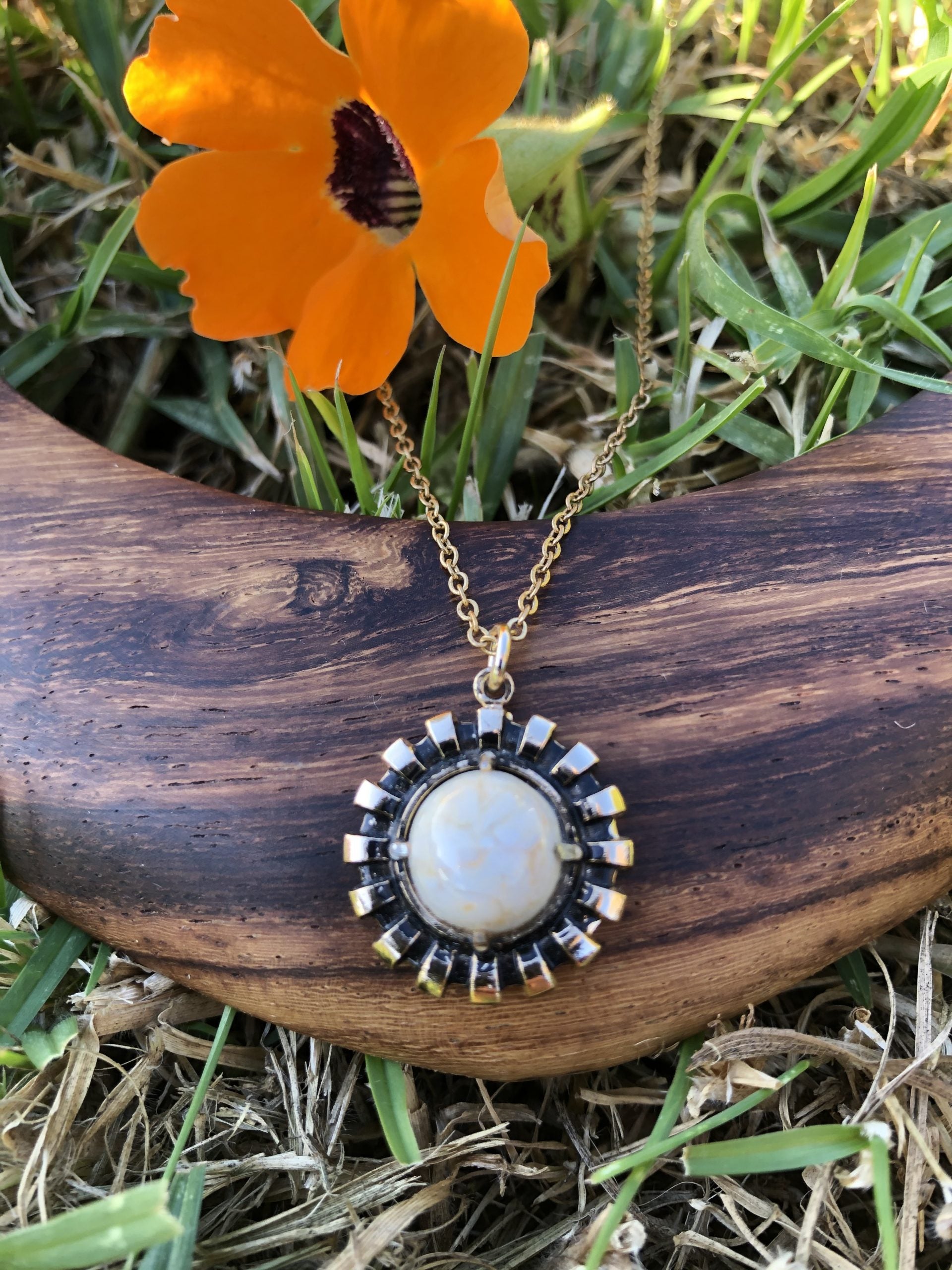 Necklace with natural New Zealand chert, white with gold lace patterns, hand polished to a 10mm round cabochon and set in a gold plated setting with 19 inch chain, on wood, bright