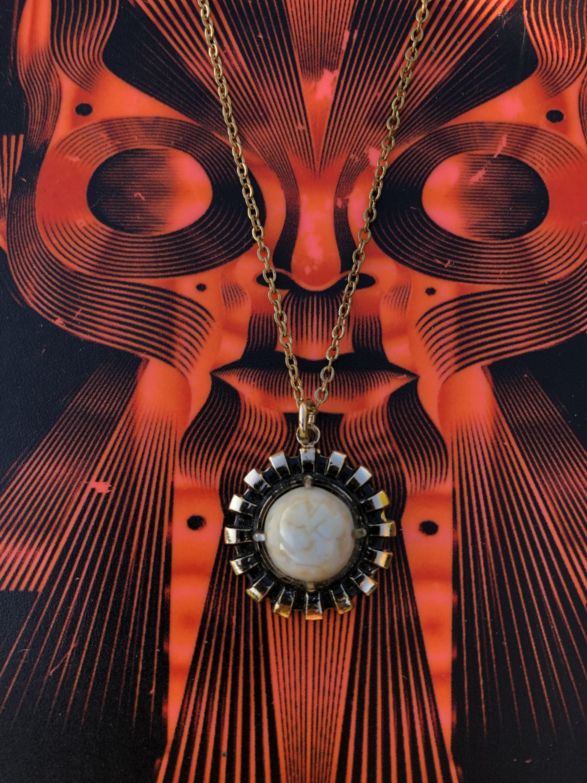 Necklace with natural New Zealand chert, white with gold lace patterns, hand polished to a 10mm round cabochon and set in a gold plated setting with 19 inch chain, on red art