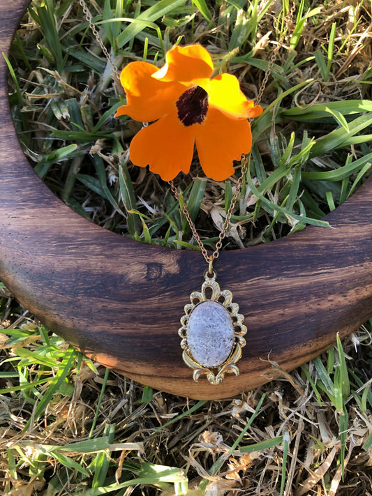 Necklace with Chrysanthemum Rhyolite from Tairua New Zealand with intricate gray and white chrysanthemum patterns, hand polished to a 15x11mm cabochon and set in a gold plated setting with 19 inch chain, on wood
