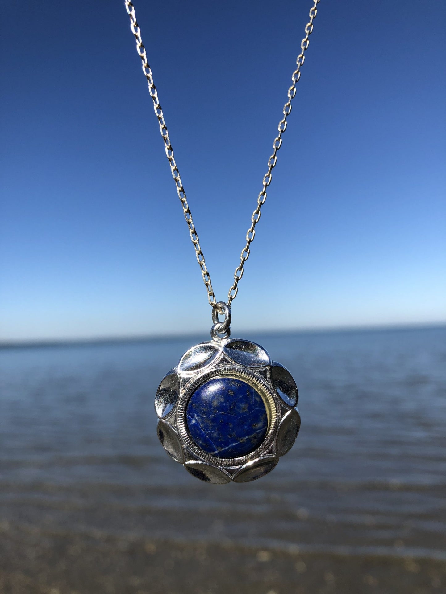 Necklace with 14mm round cabochon of natural Lapis Lazuli from Afghanistan with deep Lapis blue and some fine lines of white quarts and speckles of golden pyrites, hand polished and set in a silver-plated setting with 19 inch chain on sea