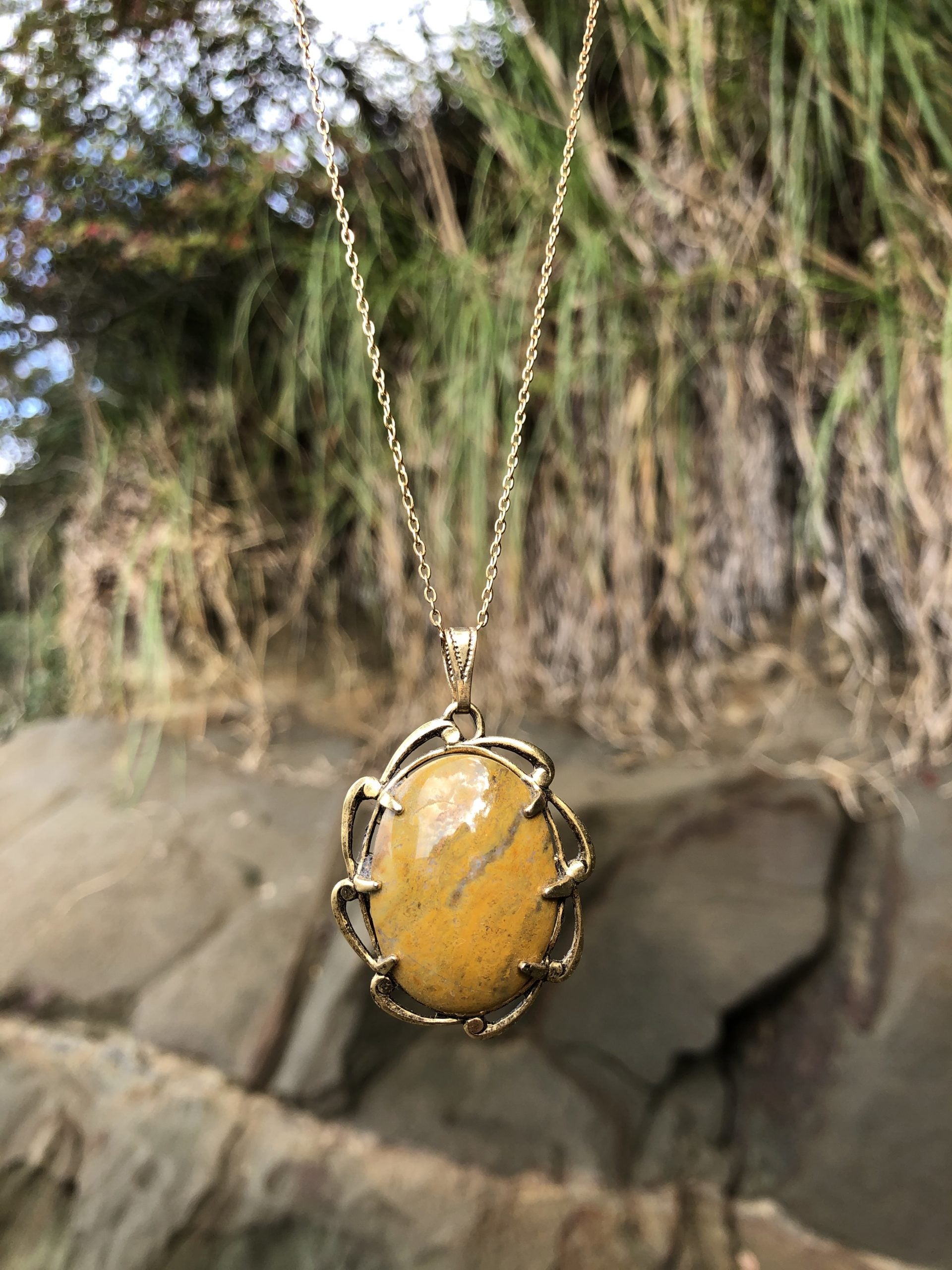 Necklace with New Zealand petrified wood, yellow with brown markings, hand polished to a 30x22mm cabochon and set in a gold plated setting with 19 inch chain, on beach