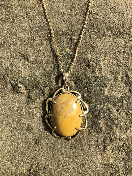 Necklace with New Zealand petrified wood, yellow with brown markings, hand polished to a 30x22mm cabochon and set in a gold plated setting with 19 inch chain, on sand