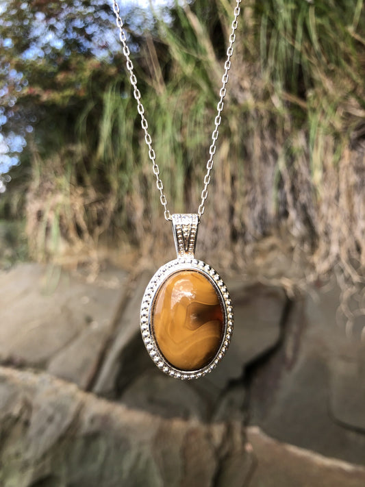 Necklace with natural New Zealand Carnelian, with sparkling translucent orange glowing through swirling browns, hand polished to a 25x18mm oval cabochon and set in a silver-plated setting with 19 inch chain, front