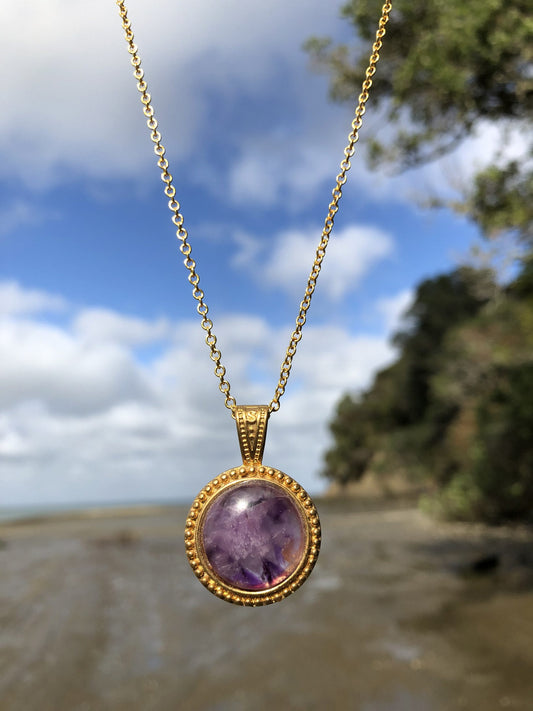 Necklace with beautiful purple Amethyst with natural color variations from crystal growth, hand polished to a 18mm round cabochon and set in a gold-plated setting with 19 inch chain, front