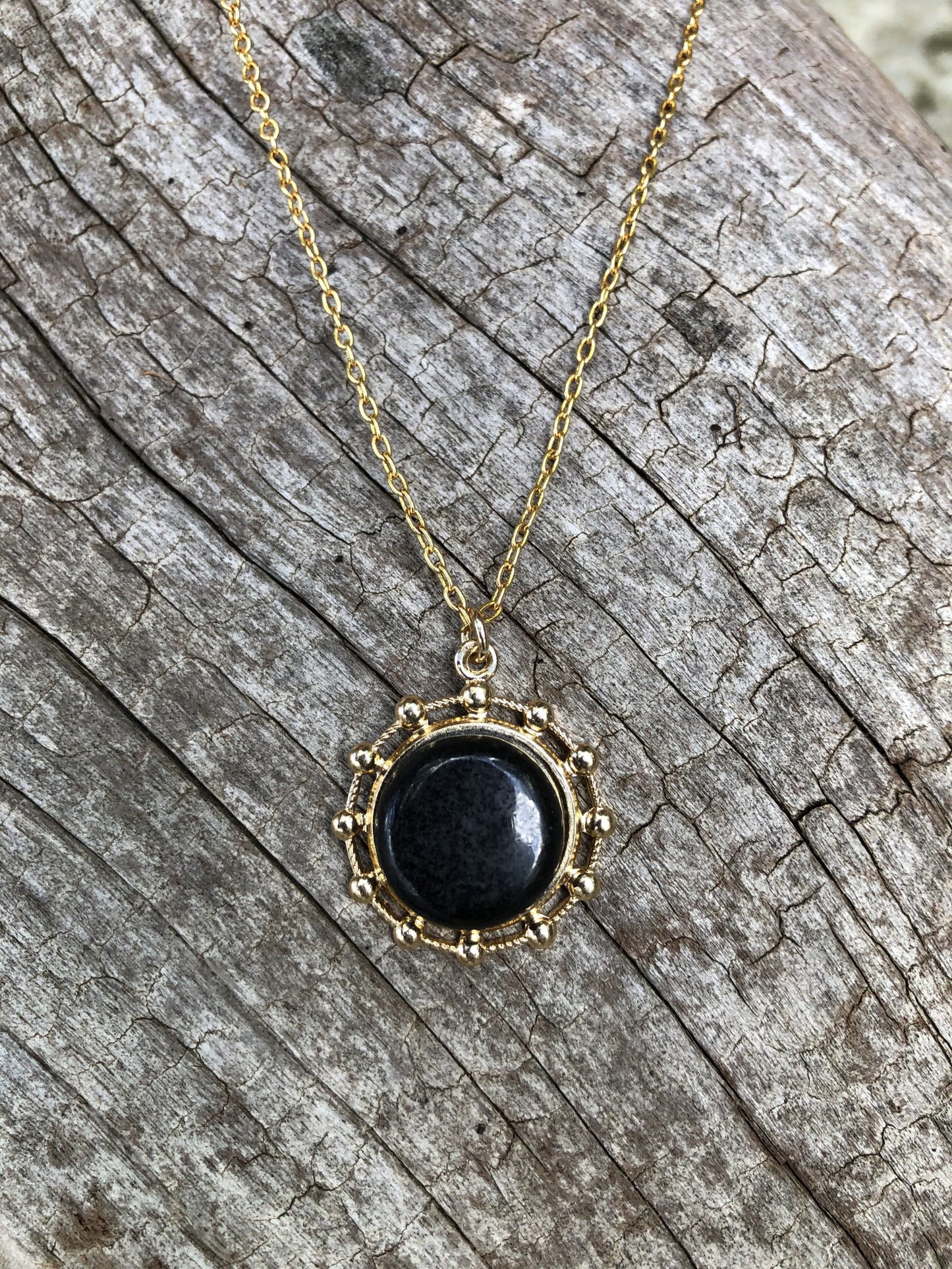 Necklace of black granite, hand polished to a 15mm disk and mounted on a gold plated setting with 19 inch chain