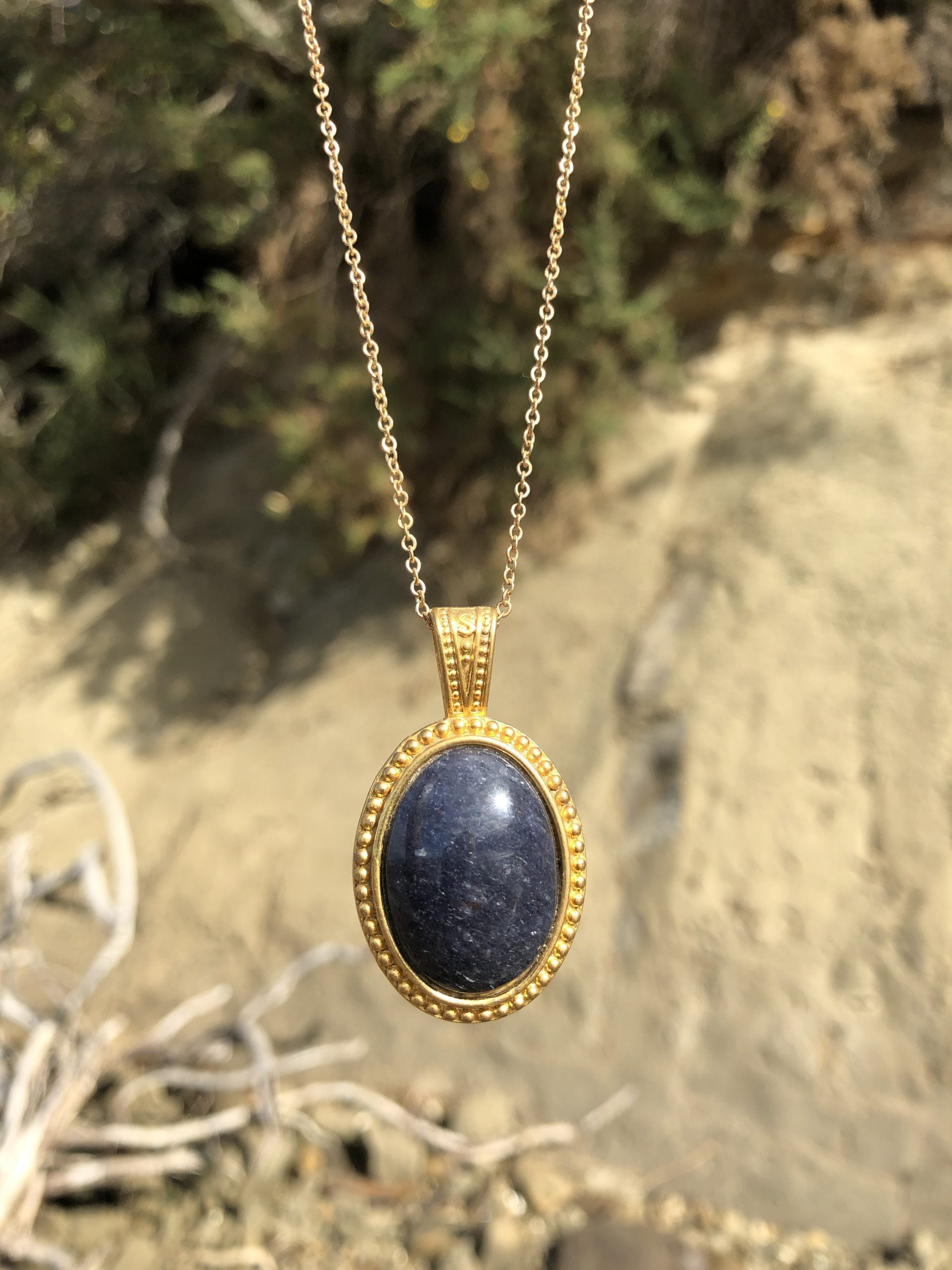 Necklace with natural blue aventurine, hand polished to a 25x18mm cabochon and set in a gold plated setting with 19 inch chain, on beach