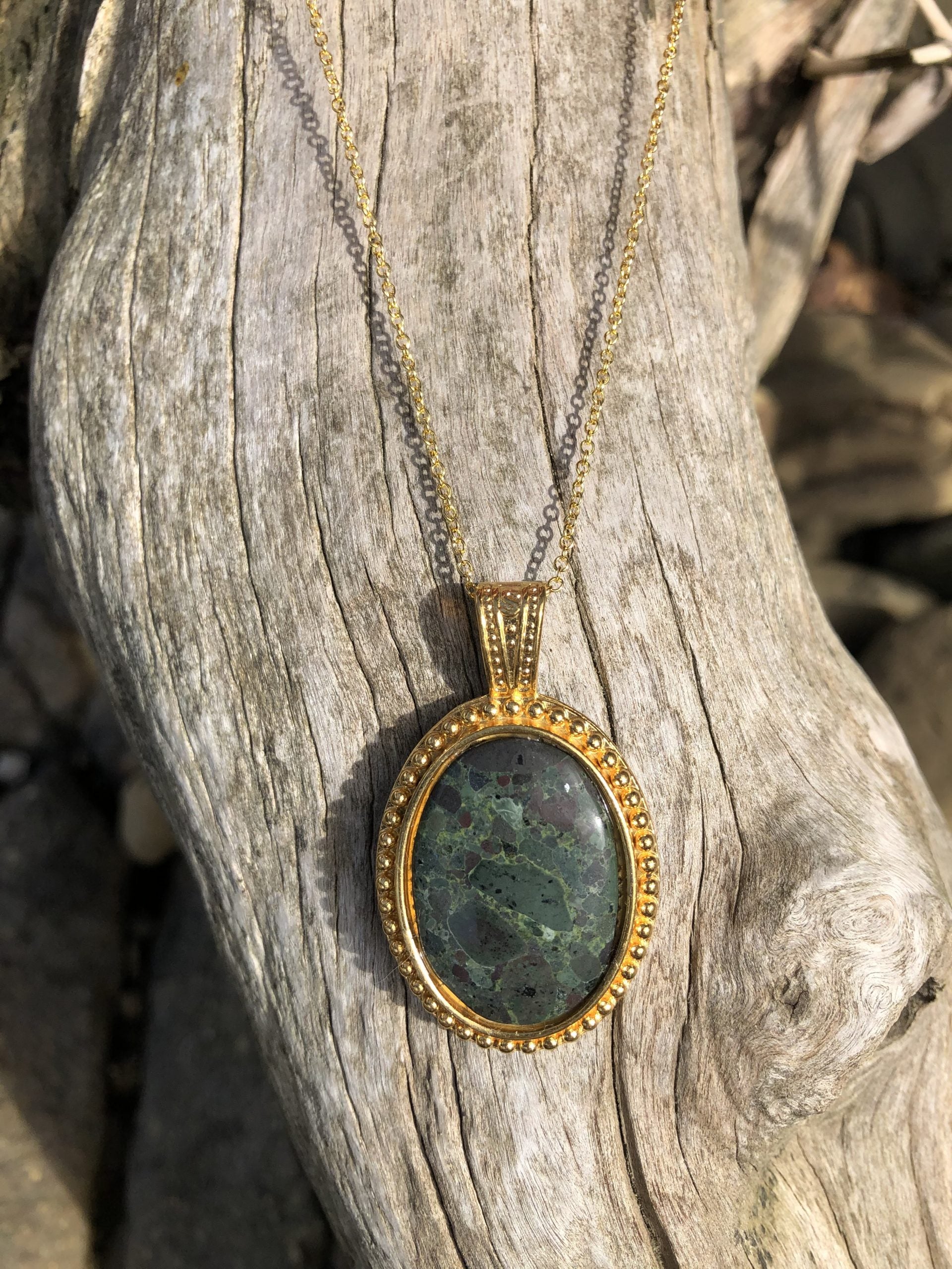 Necklace, green brecciated rhyolite from Coromandel NZ, hand polished into a 30x20mm cabochon and set in gold plated setting with 19 inch chain on tree background 