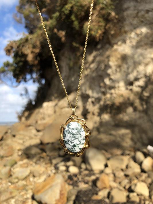 Necklace with natural Tree Agate, a unique type of moss agate with a white background behind fine green "moss". The stone is hand polished to a 25x18mm cabochon and set in a gold plated setting with 19 inch chain, on beach