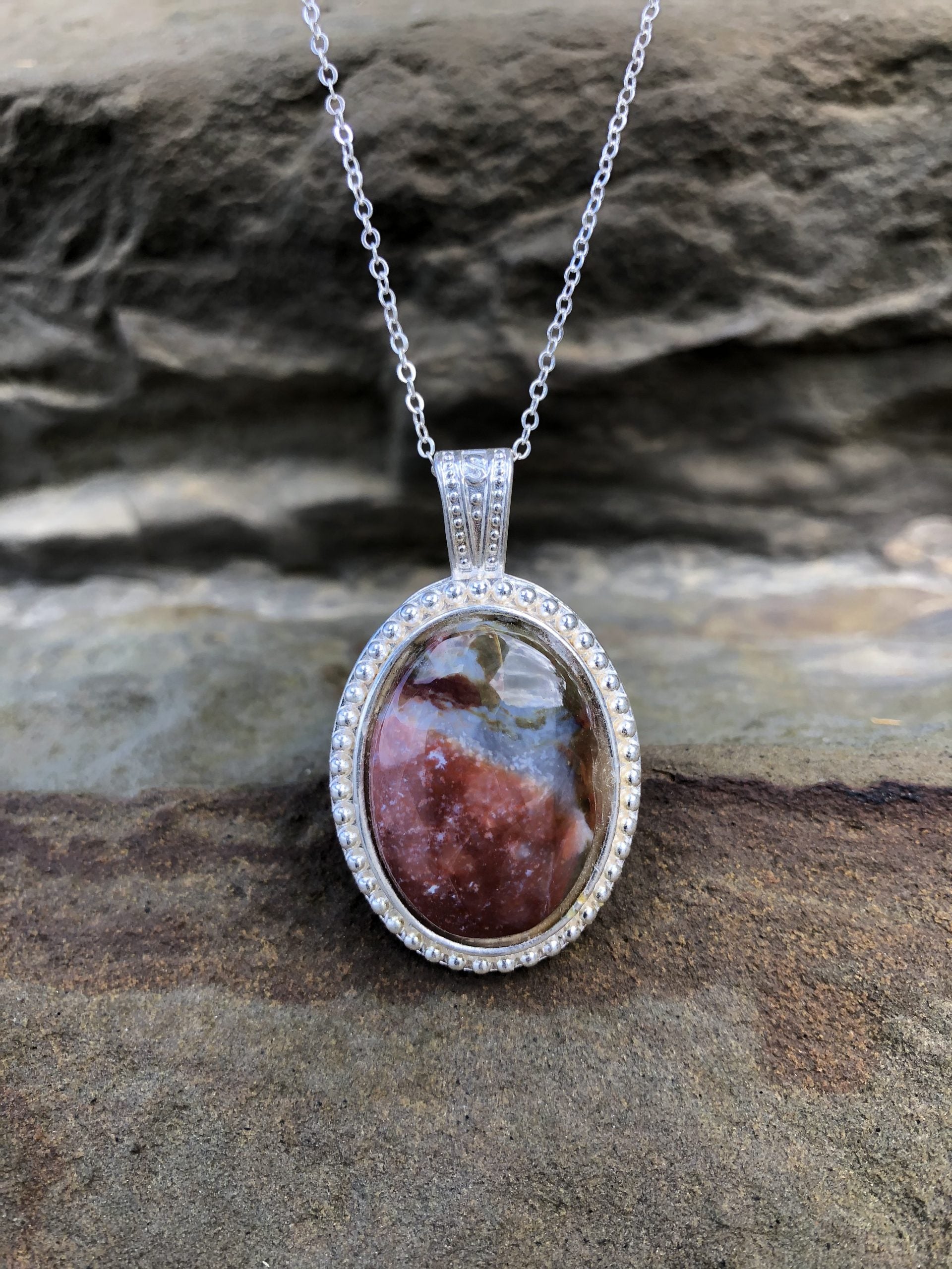 Necklace with a natural jasper-agate from the Hotoritori stream in the Kauranga valley with red, white and brown, hand polished to a 25x18mm cabochon and set in a silver plated setting with 19 inch chain, on stone