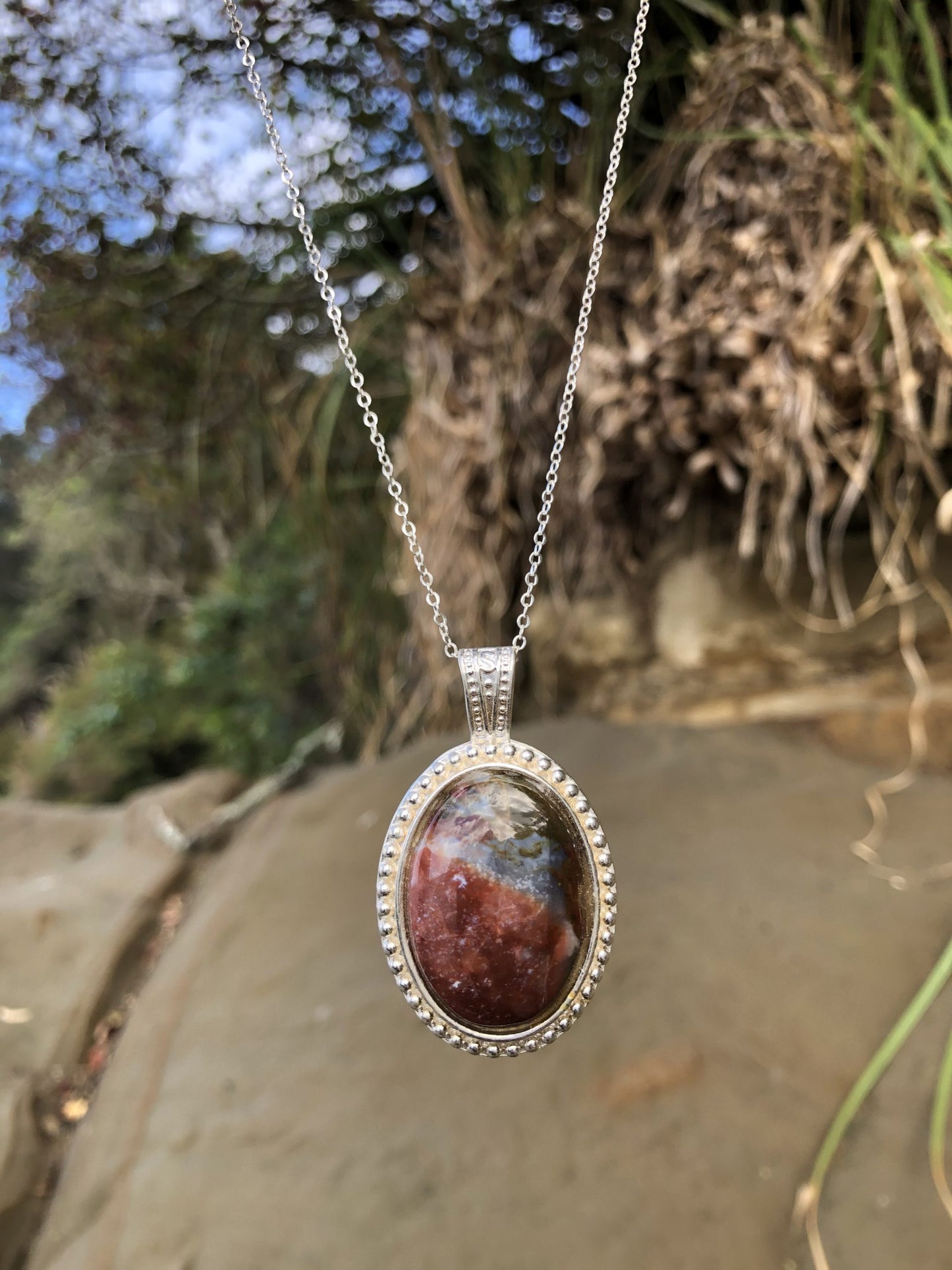 Necklace with a natural jasper-agate from the Hotoritori stream in the Kauranga valley with red, white and brown, hand polished to a 25x18mm cabochon and set in a silver plated setting with 19 inch chain, on beach