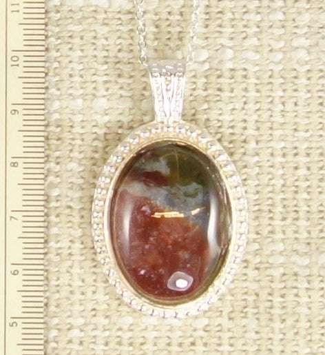 Necklace with a natural jasper-agate from the Hotoritori stream in the Kauranga valley with red, white and brown, hand polished to a 25x18mm cabochon and set in a silver plated setting with 19 inch chain, on burlap
