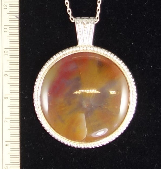 Necklace of Arizona petrified "rainbow" wood, named for its beautiful colors including red, yellow and orange. This is a 40mm round cabochon, hand cut to show the center of the branch and radiating growth rings, set in silver plated setting with 19 inch chain