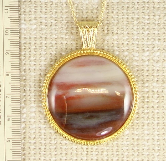 Necklace of petrified wood from USA with reds and whites, cut into a 40mm round cabochon and set in gold plated setting with 19 inch chain.